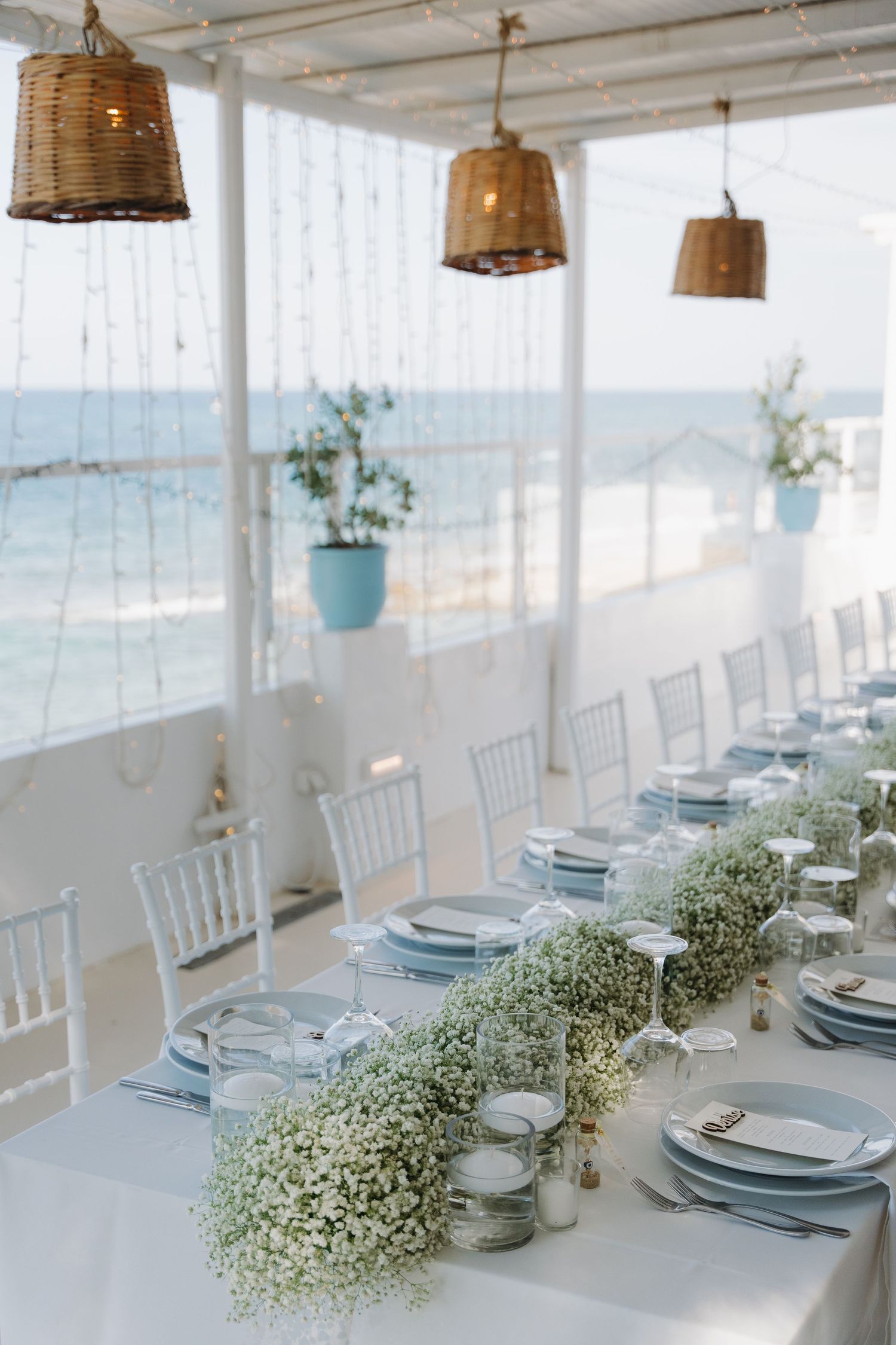Elegant white coastal wedding reception setup with rustic pendant lights and ocean view.