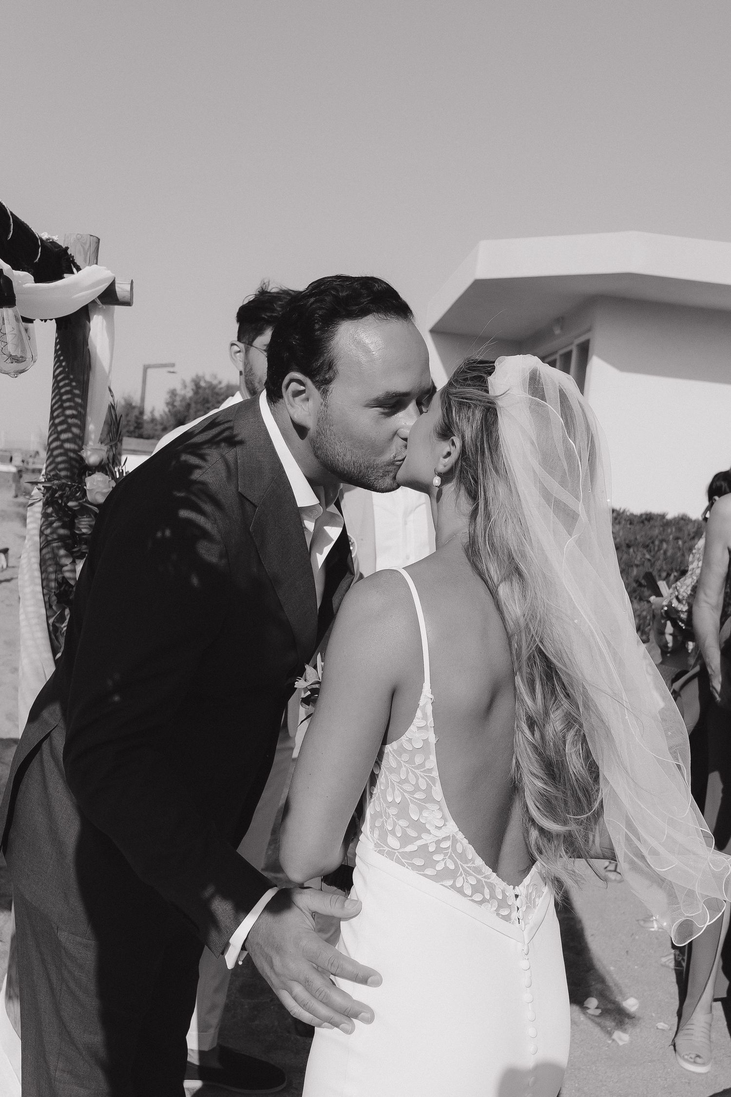Black and white photo of a romantic kiss between newlyweds during an outdoor ceremony.