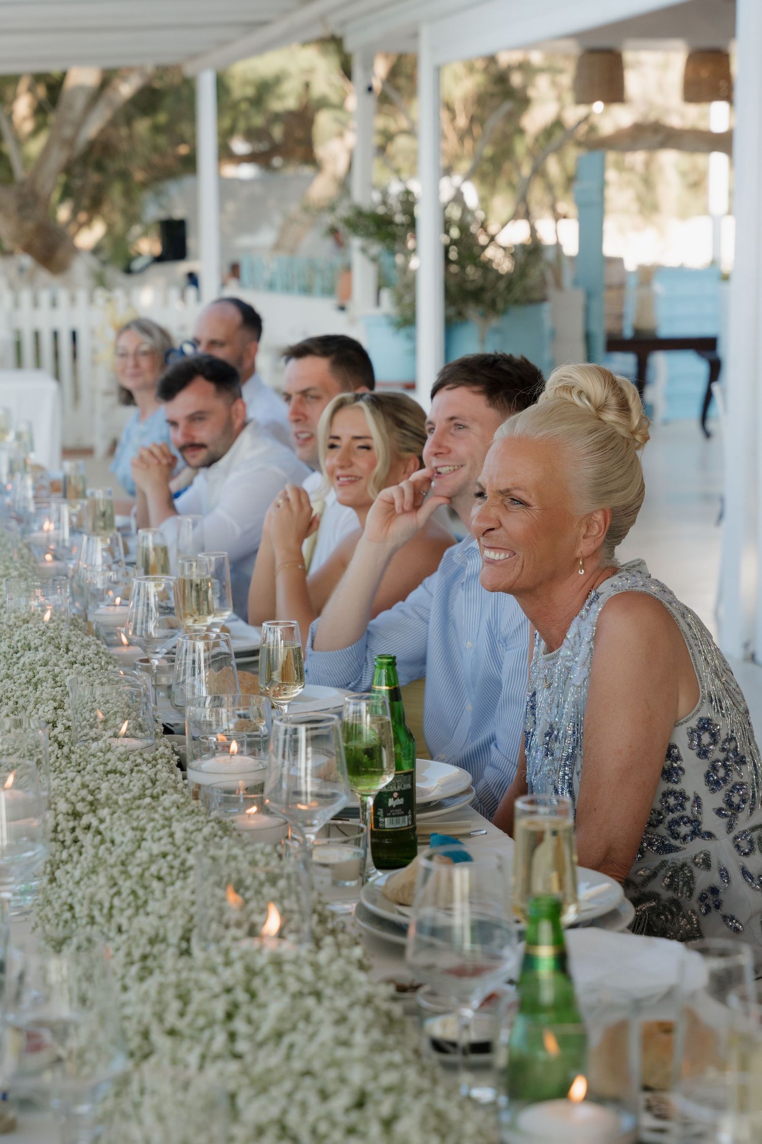 Wedding guests seated at an elegant reception table decorated with baby's breath flowers and candles at an outdoor venue.
