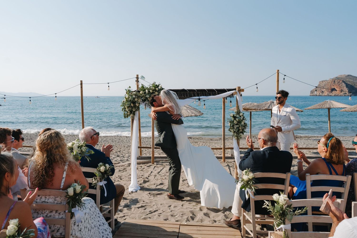 A beachside wedding ceremony setup with wooden chairs and floral arch overlooking the ocean.