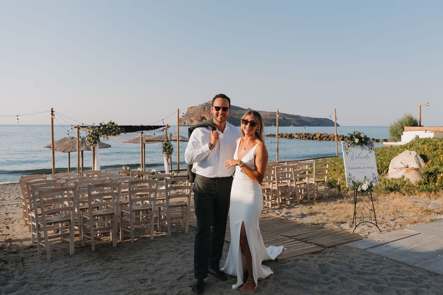 Wedding couple posing for photos at rustic beach venue with wooden fence and ocean views.