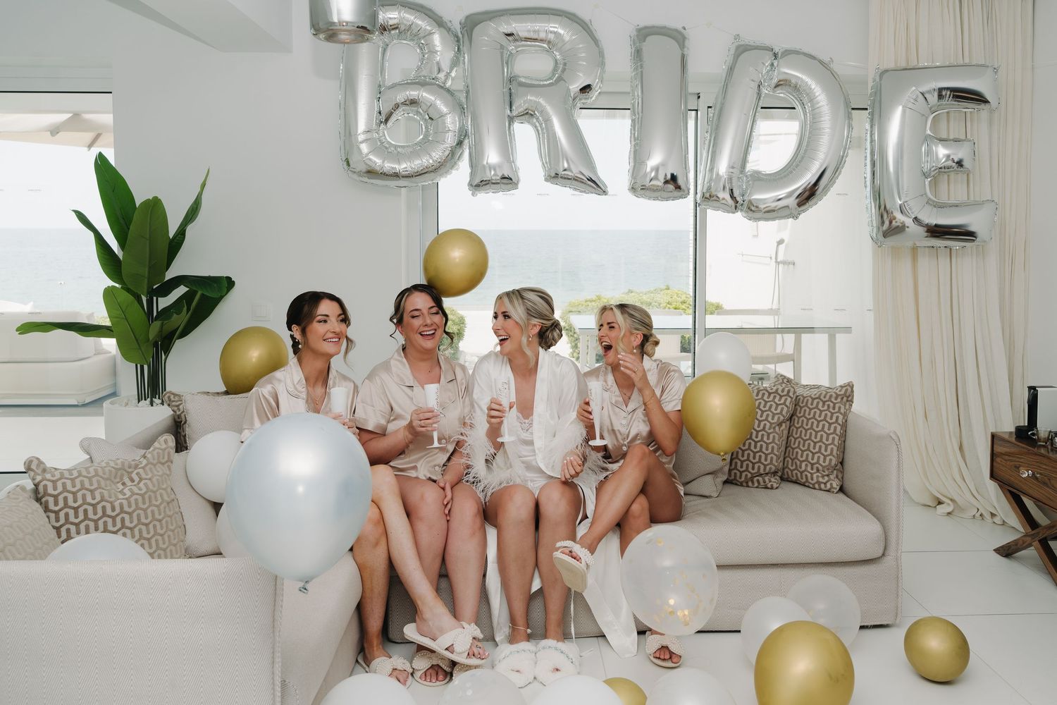Bridal party celebrating with silver letter balloons and gold accents in a modern living room.