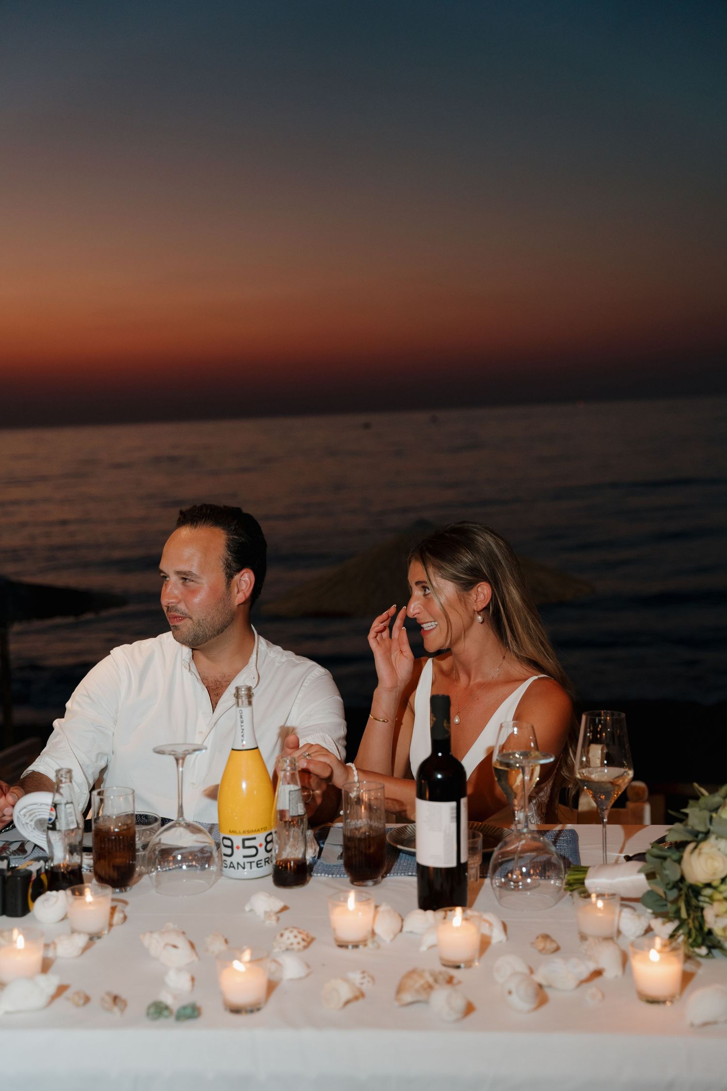 Intimate beach dinner setting at sunset with candles, wine and ocean views.