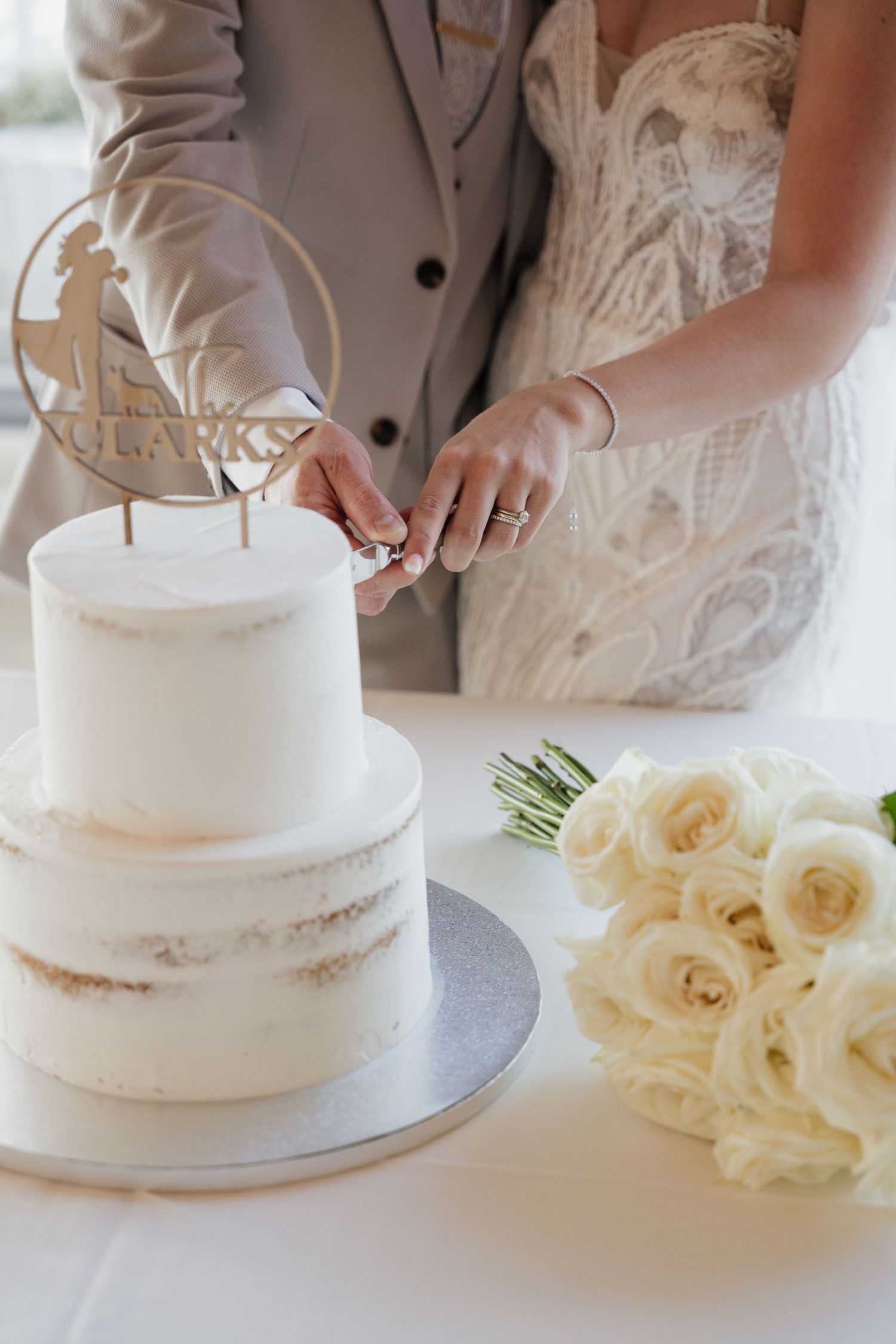 Elegant white two-tiered wedding cake with cake topper and cream roses on display at reception.