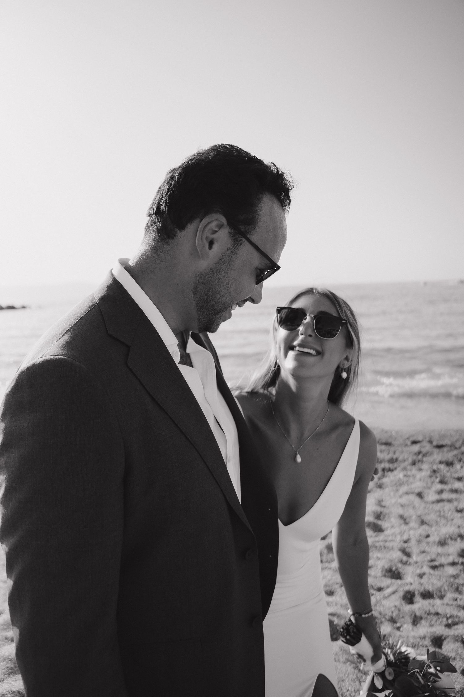 A black and white portrait of a couple sharing a candid moment on the beach.