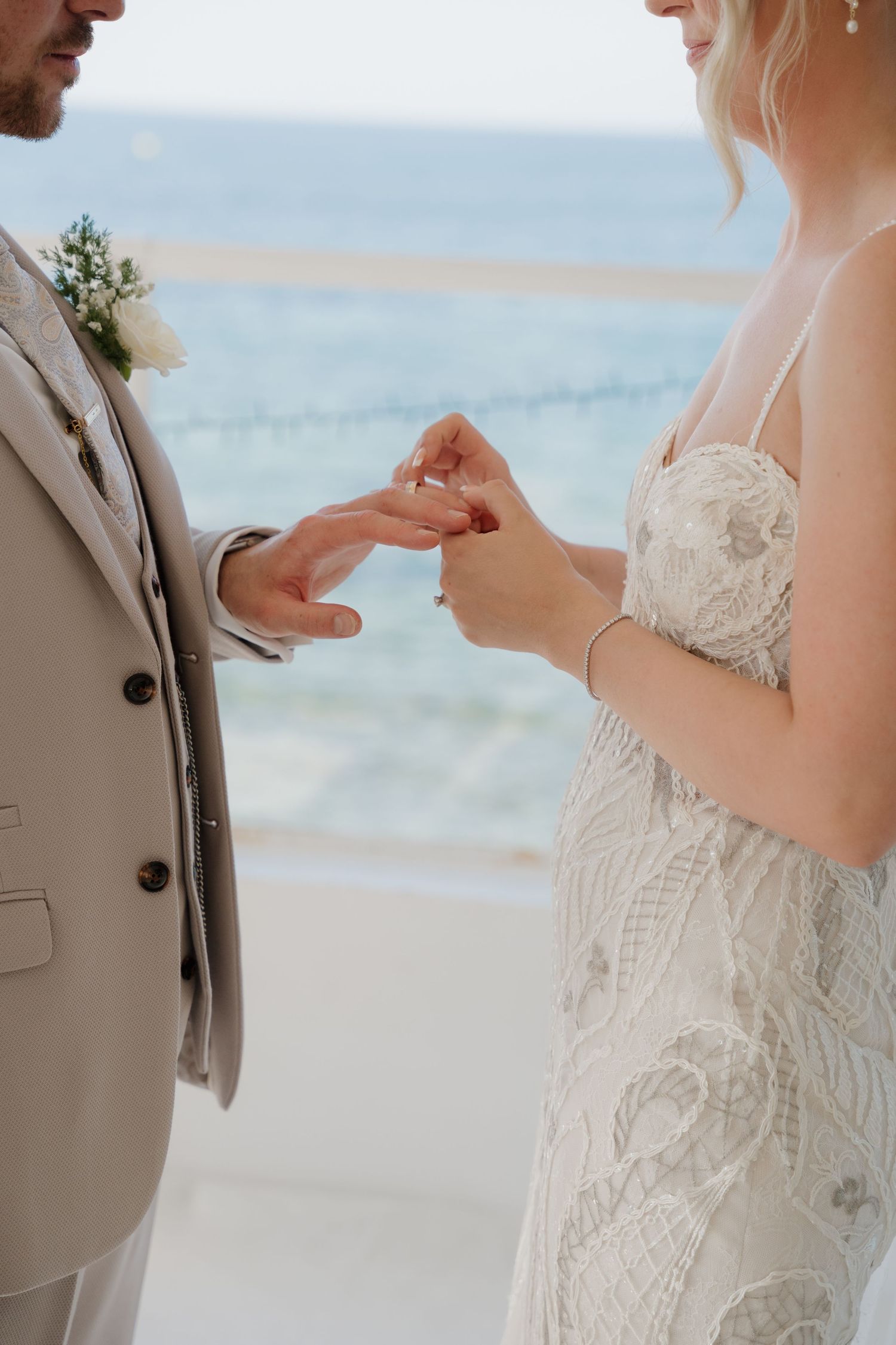 Close-up of hands exchanging rings during a beach wedding ceremony with ocean waves in background.