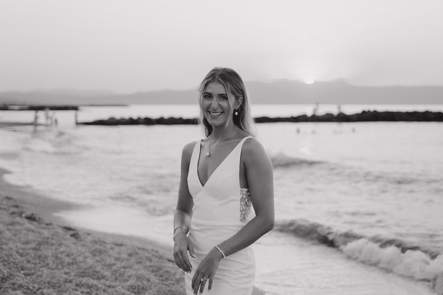 Black and white portrait of bride on beach at sunset with serene coastal backdrop.