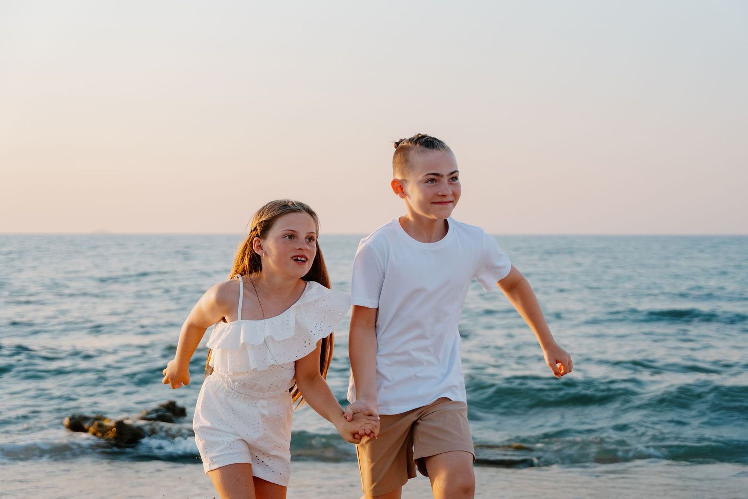 Playful beach scene with running and laughter against ocean waves at sunset.