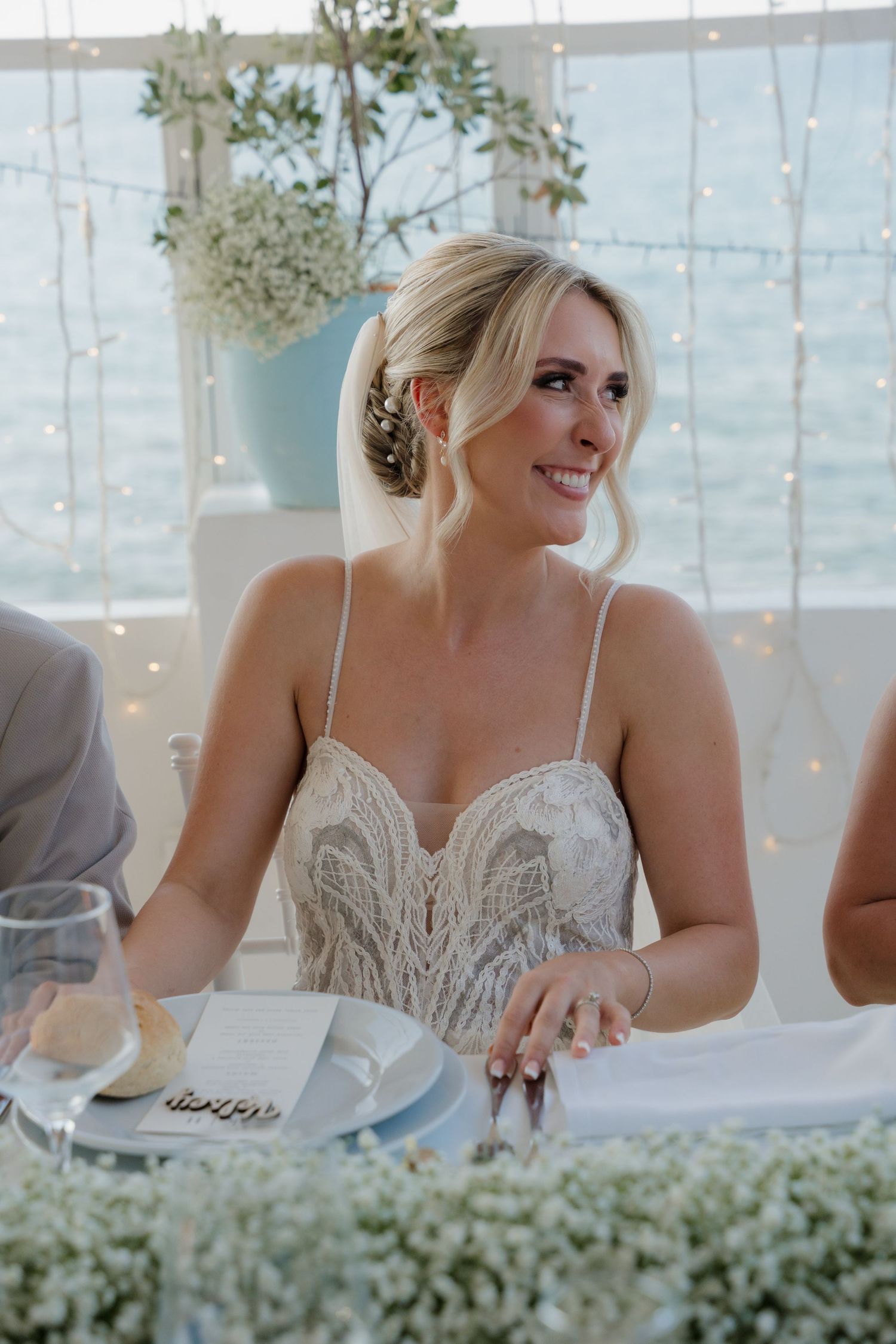 A wedding reception guest smiles while seated at an elegantly decorated table with ocean views.