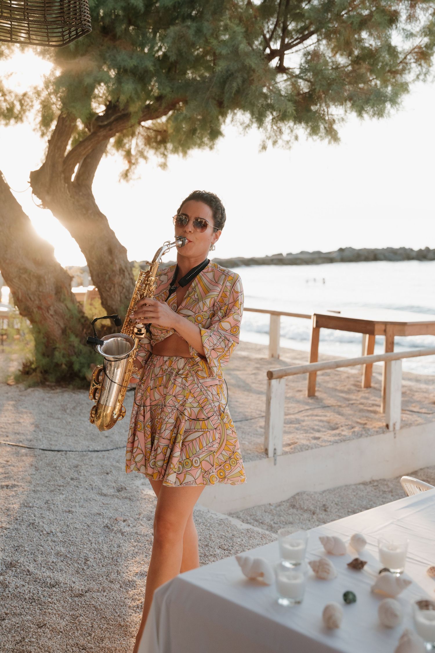 Musician plays saxophone at sunset beach wedding reception.