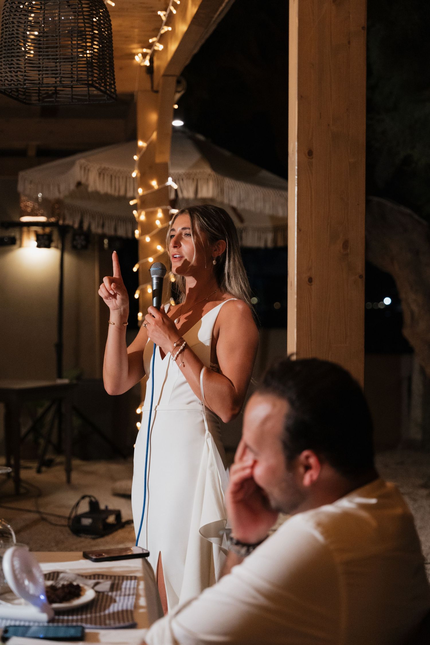 Wedding reception speech moment under wooden beams with string lights.