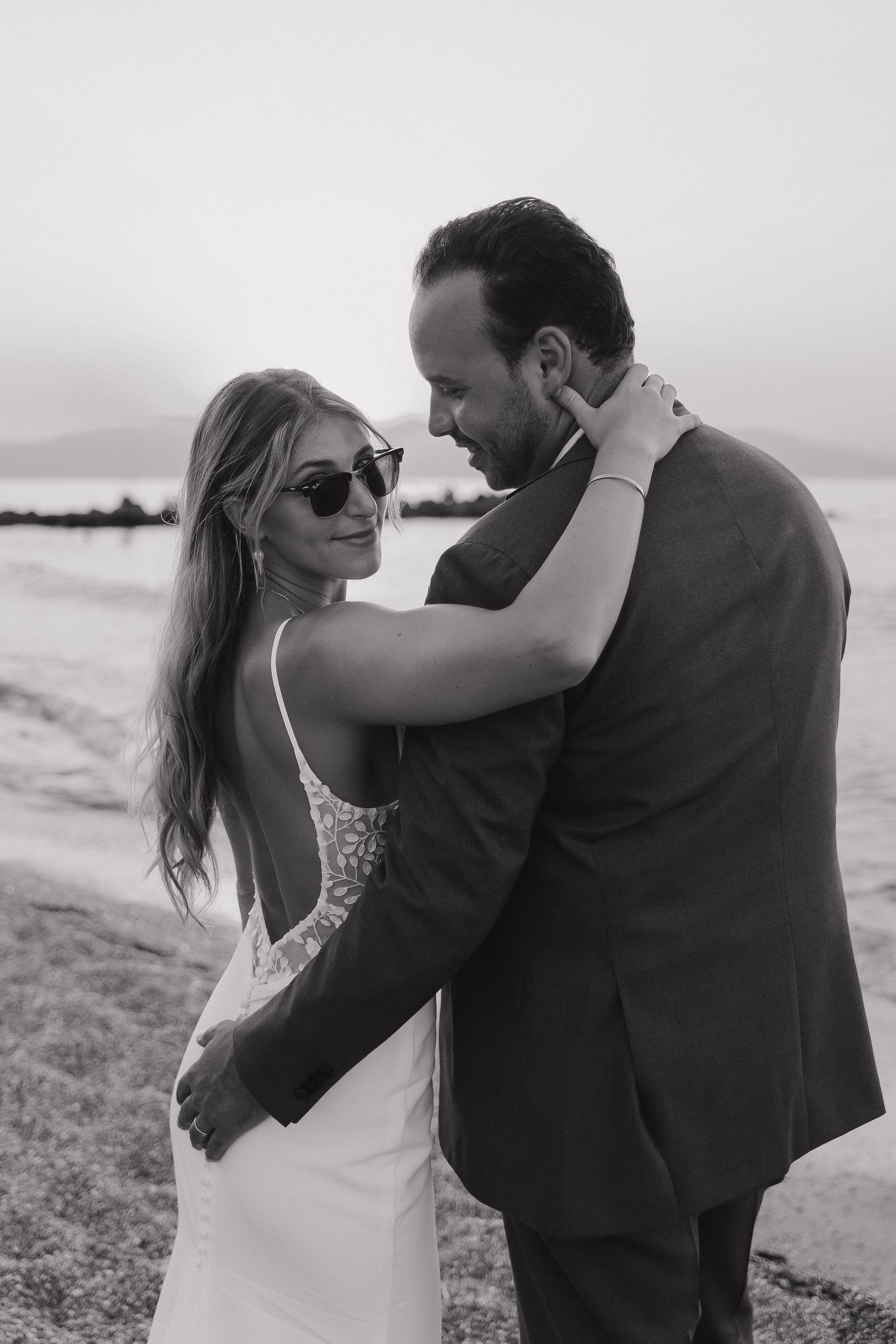 Black and white portrait of couple embracing on beach in formal wedding attire.