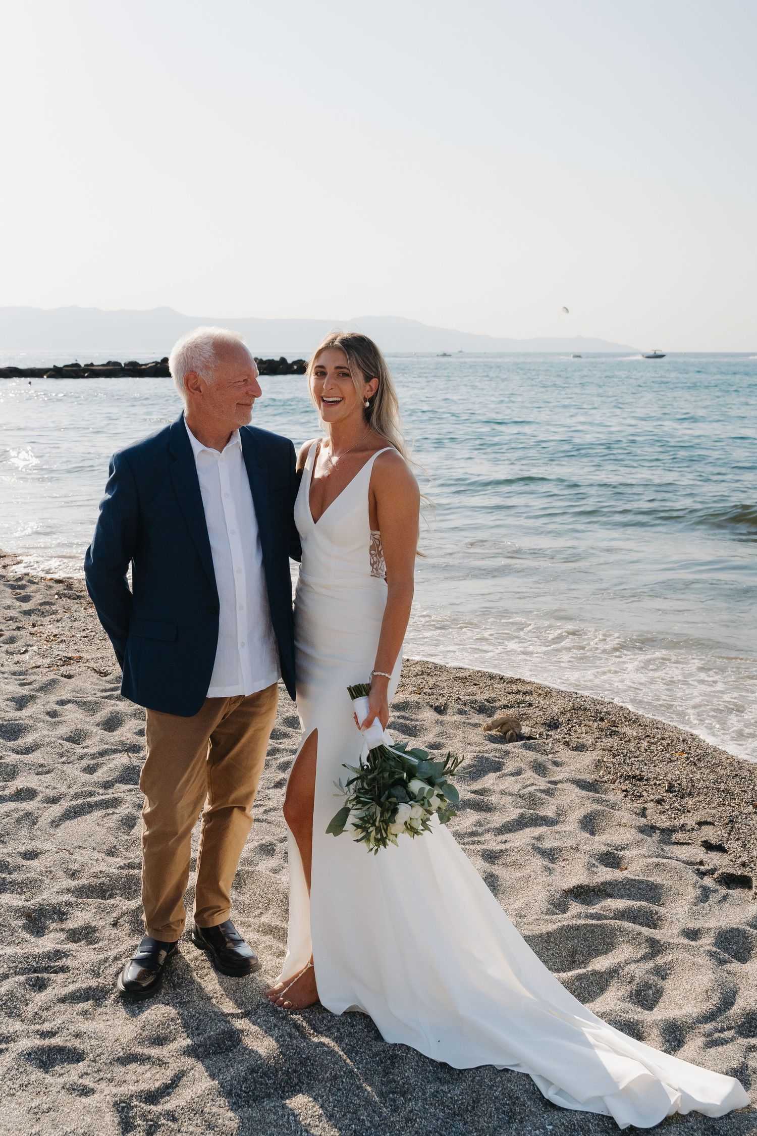 Elegant beach wedding photos with couple and guests posing on sandy shoreline at sunset.
