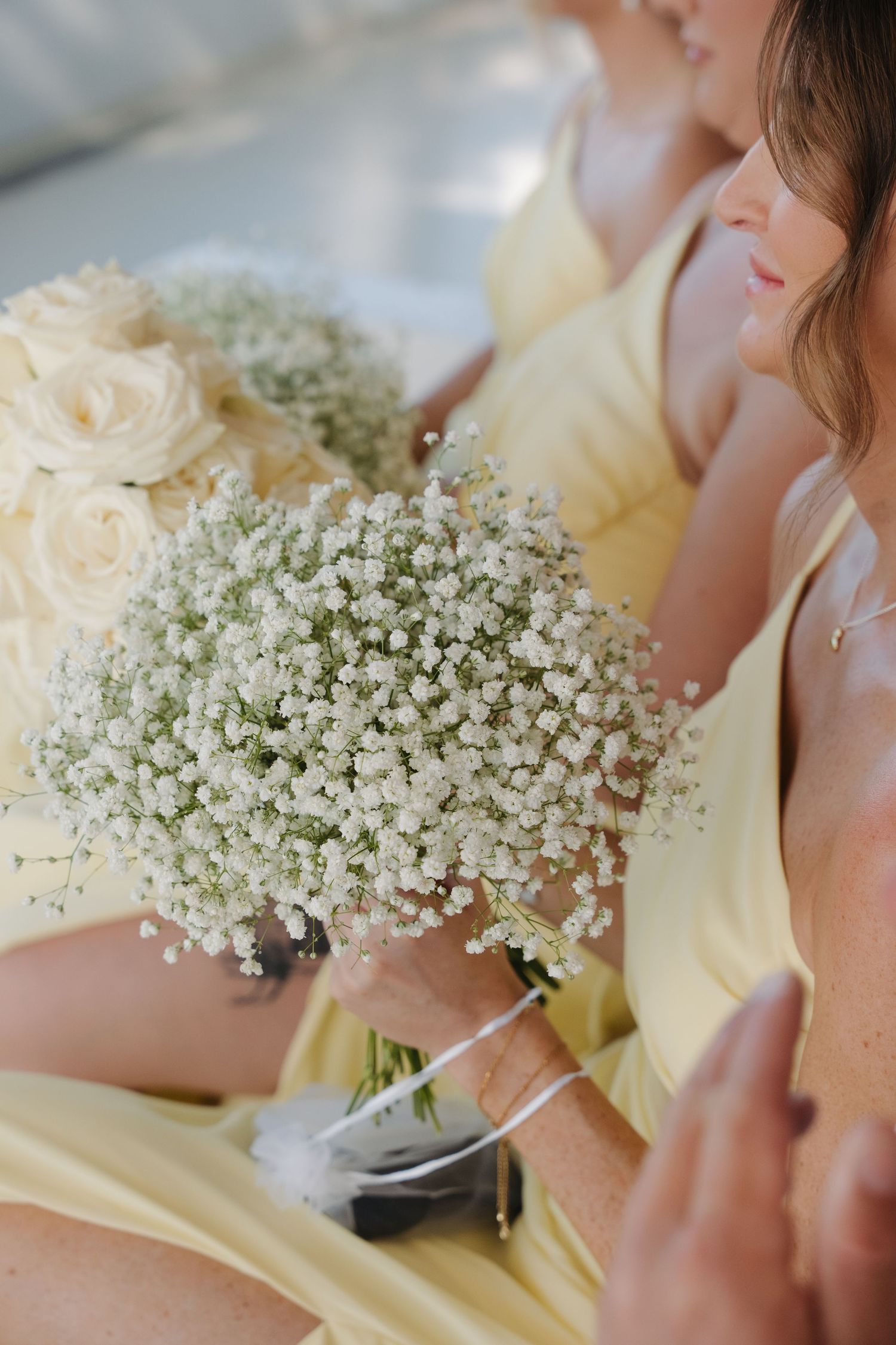 Bridesmaid in pale yellow dress holding delicate baby's breath and white rose bouquet at wedding ceremony.
