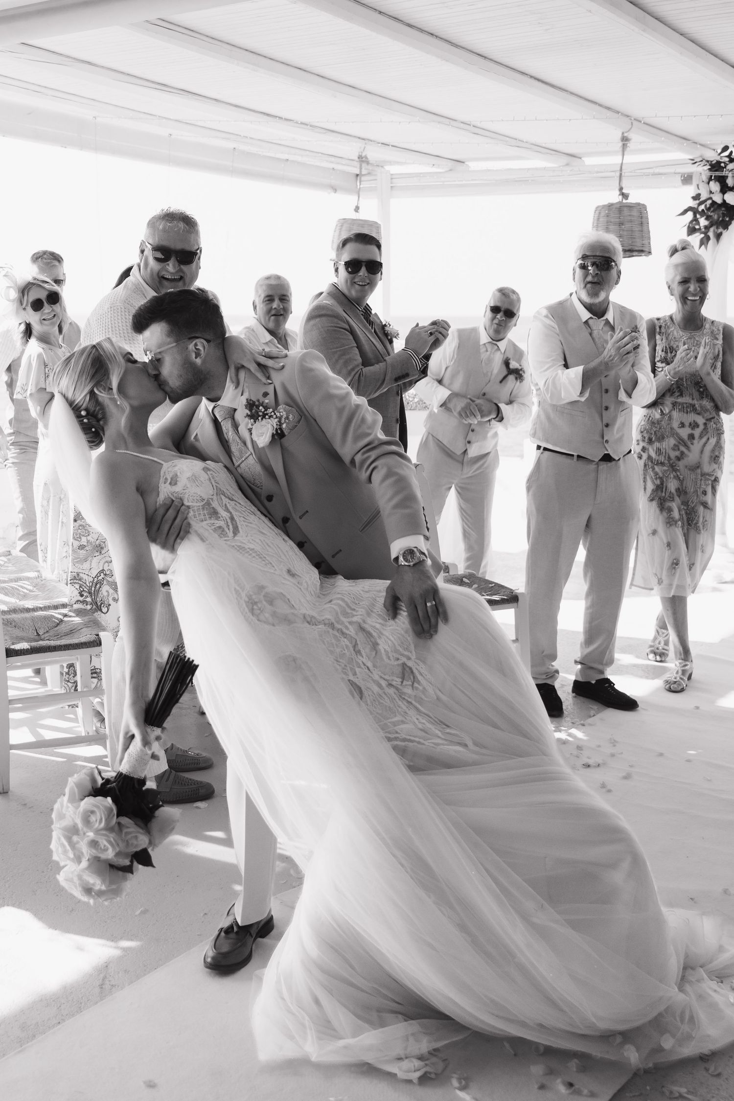 Wedding party dances and celebrates on a covered outdoor terrace overlooking the ocean.