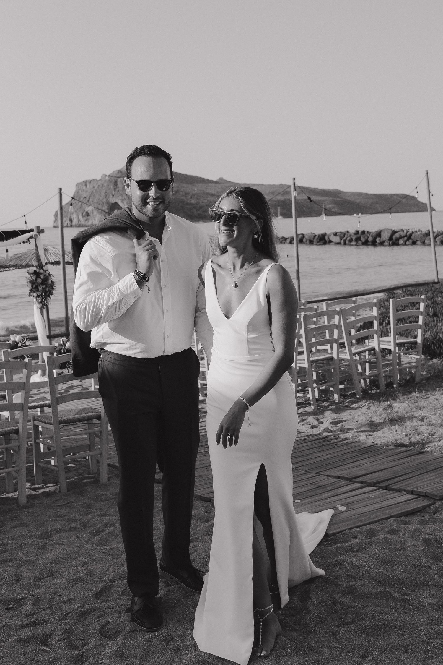 A couple wearing sunglasses pose together at an outdoor wedding venue with mountain views in the background.