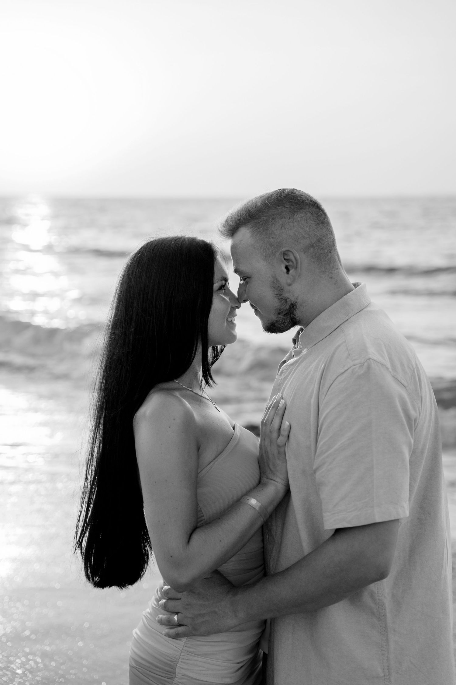 A black and white intimate portrait of a couple on the beach at sunset.