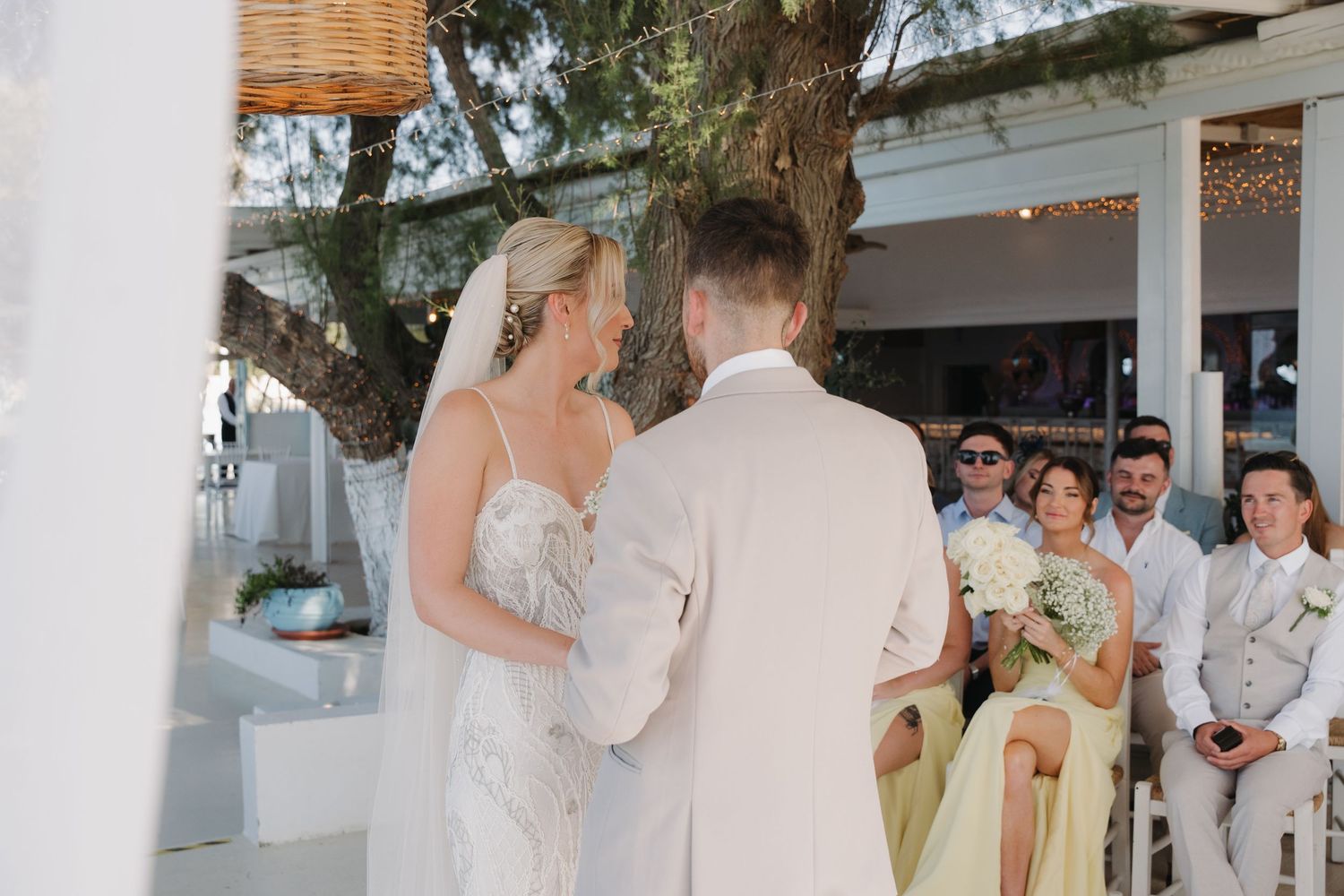 Wedding ceremony in progress under white pergola with guests watching.