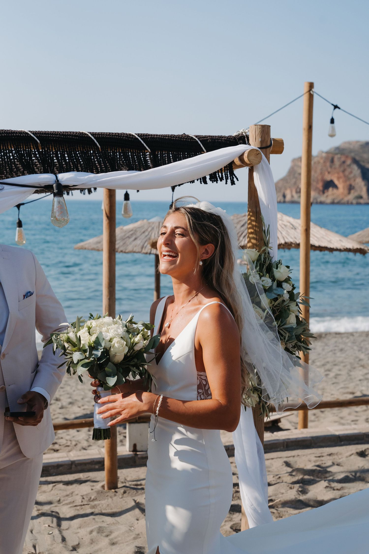 A beach wedding ceremony setup with wooden posts and white fabric overlooking the ocean on a sunny day.