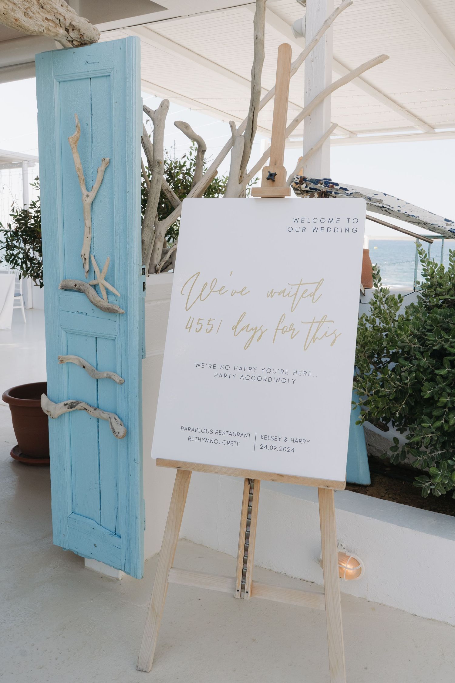 Wedding welcome sign on white easel with blue vintage door and greenery decor.