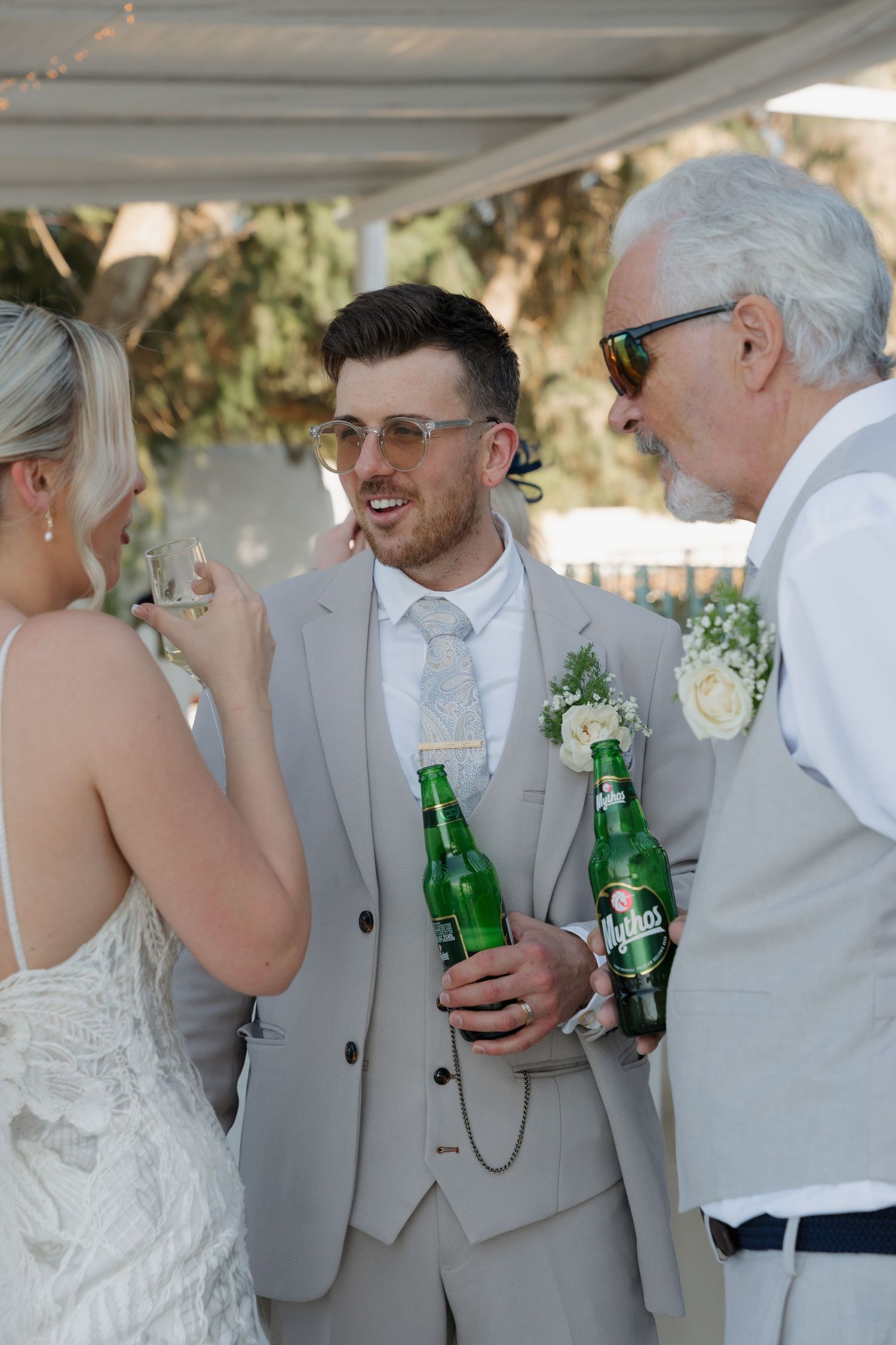 Wedding guests enjoying drinks and conversation under a covered outdoor setting.