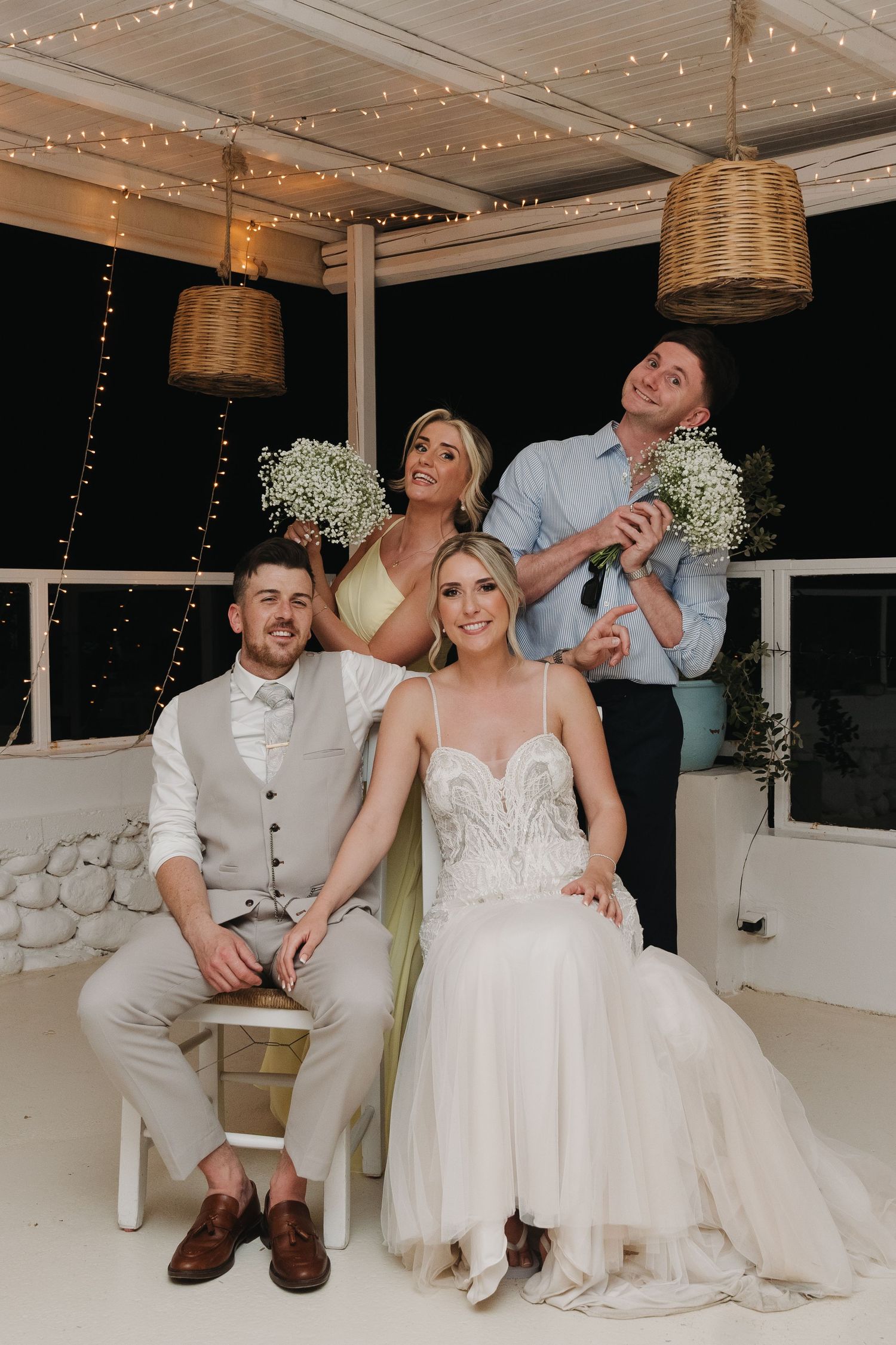 Candid wedding portrait of couple and family members under wicker pendant lights.