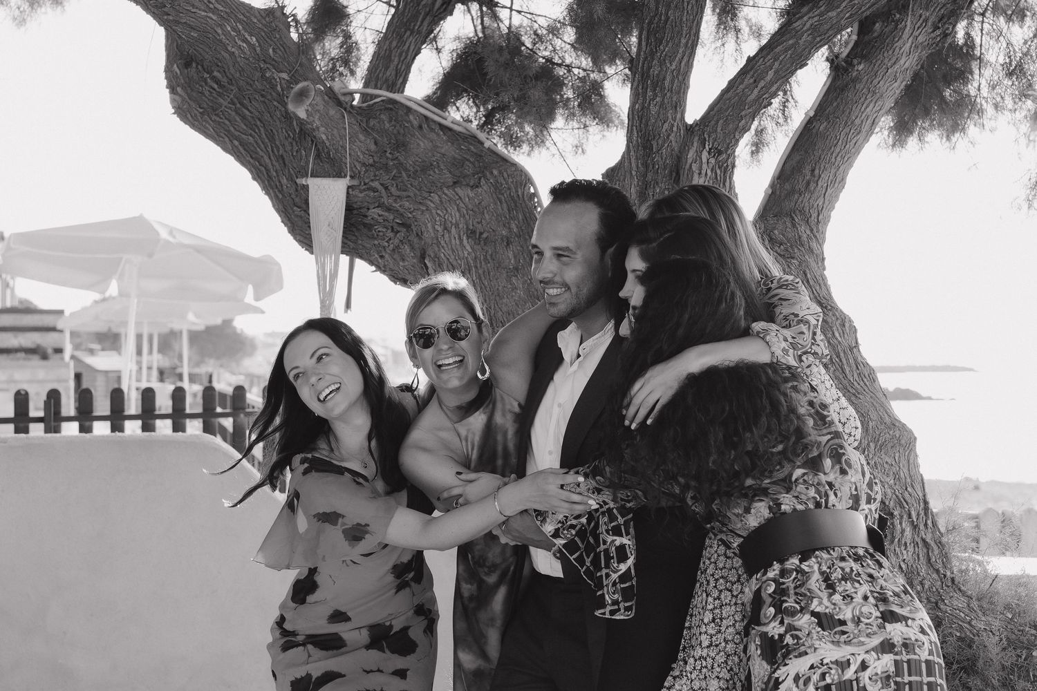 Black and white group photo of friends celebrating under a tree outdoors.