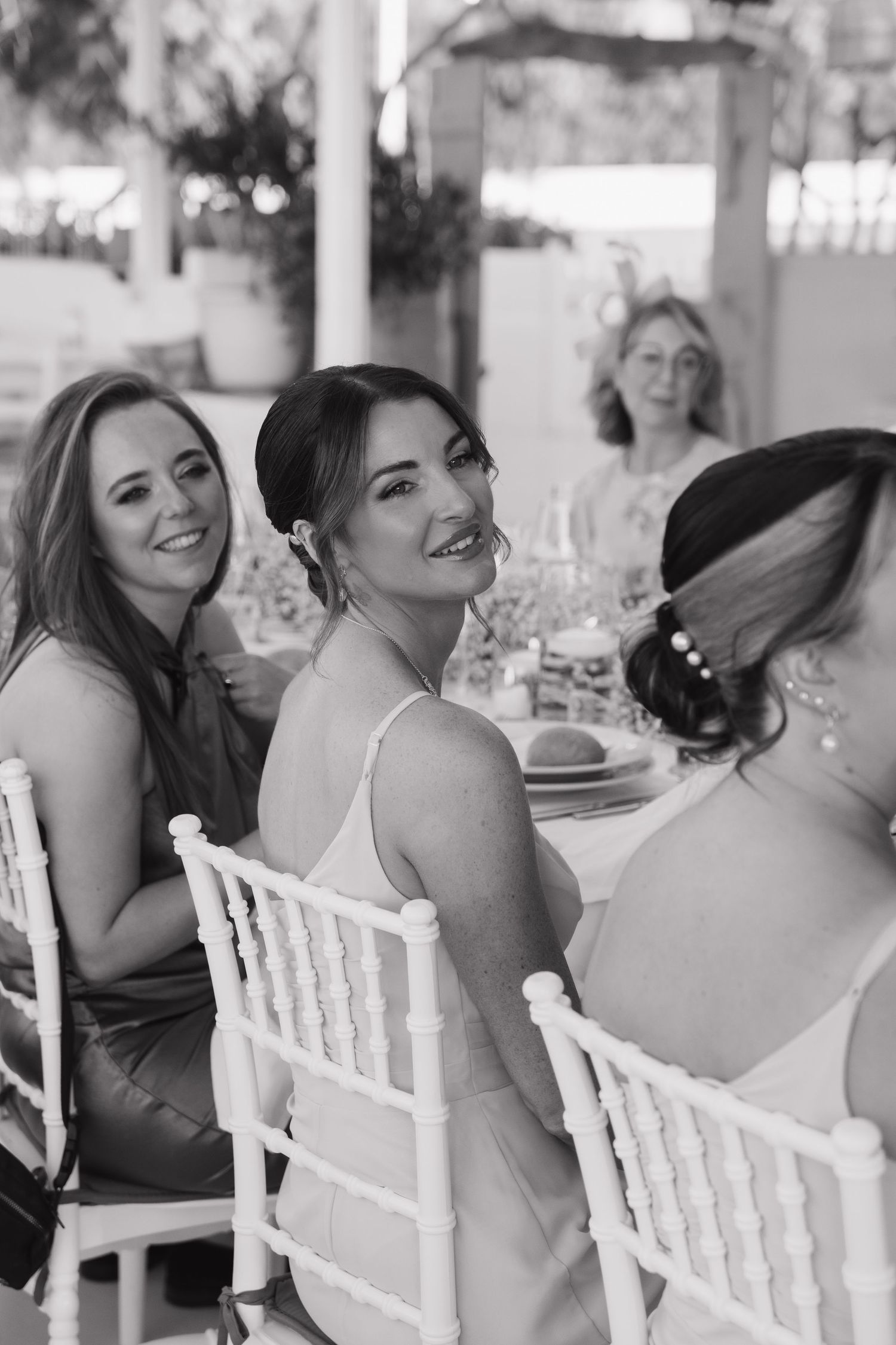 Wedding guests share laughs while seated at white chairs during the reception.