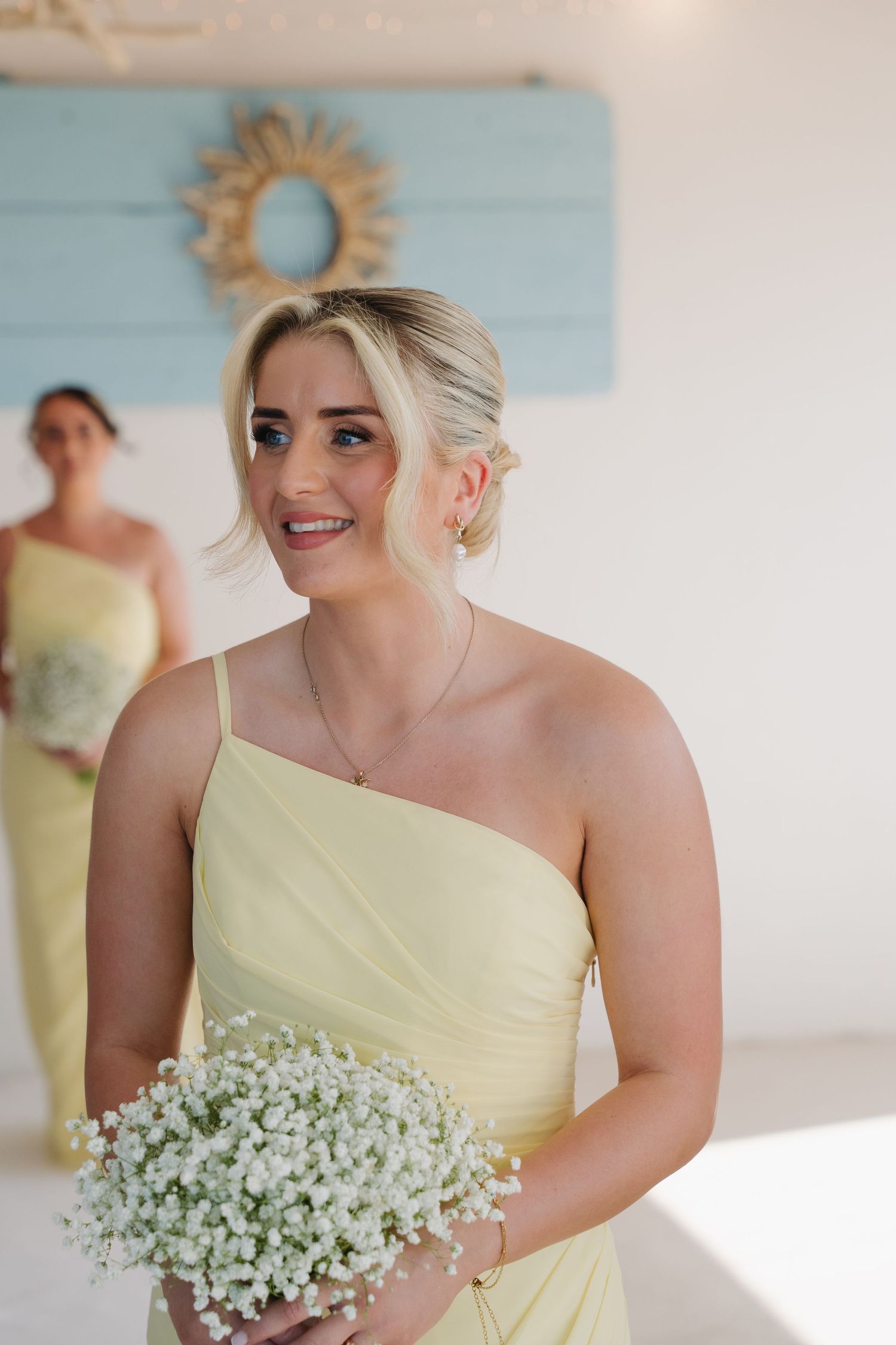 Bridesmaid in yellow one-shoulder dress holds baby's breath bouquet.