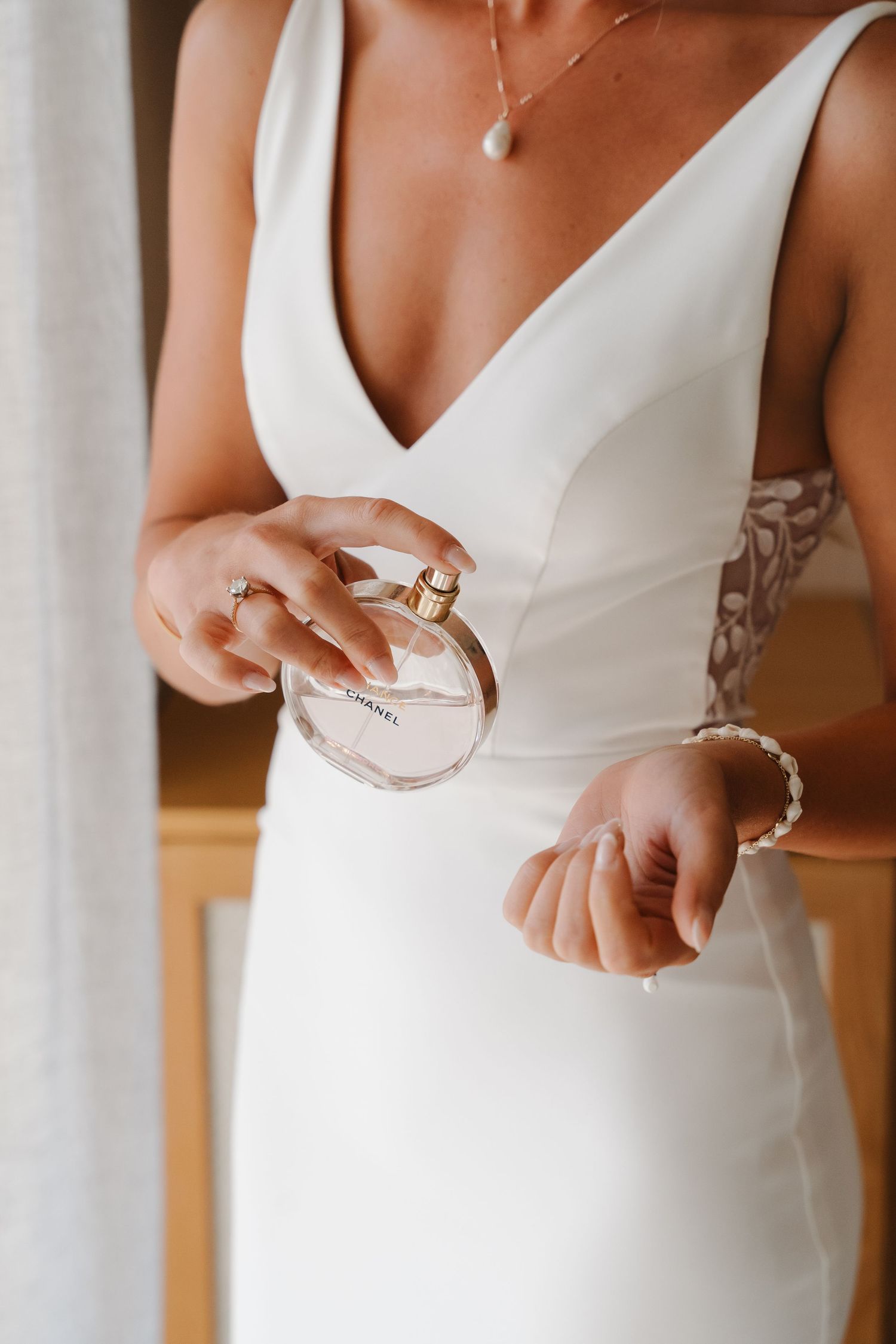 A close-up shot of a bride in a white dress holding a perfume bottle, with delicate jewelry details.