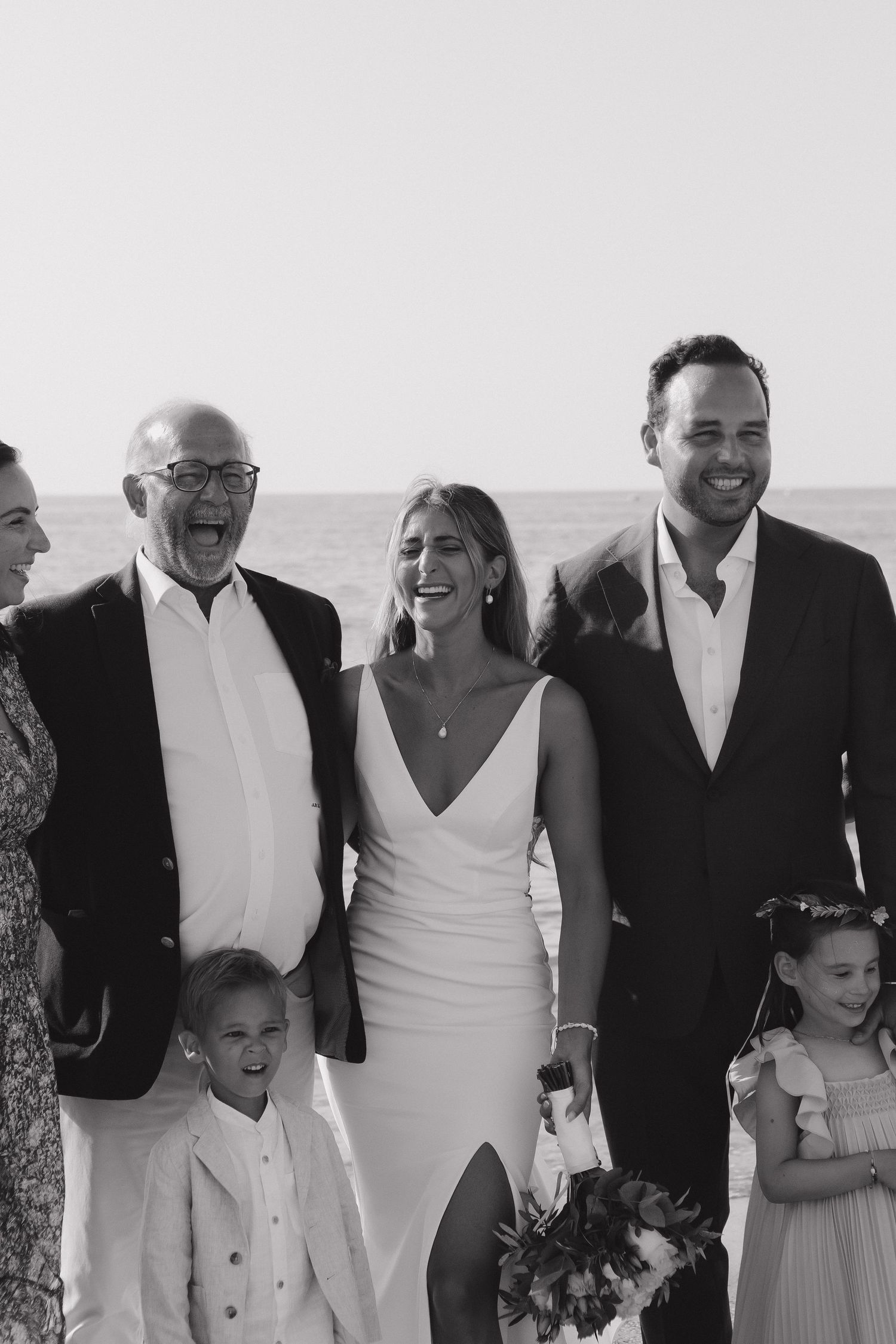 Black and white group photo showing wedding party and family members smiling together outdoors.