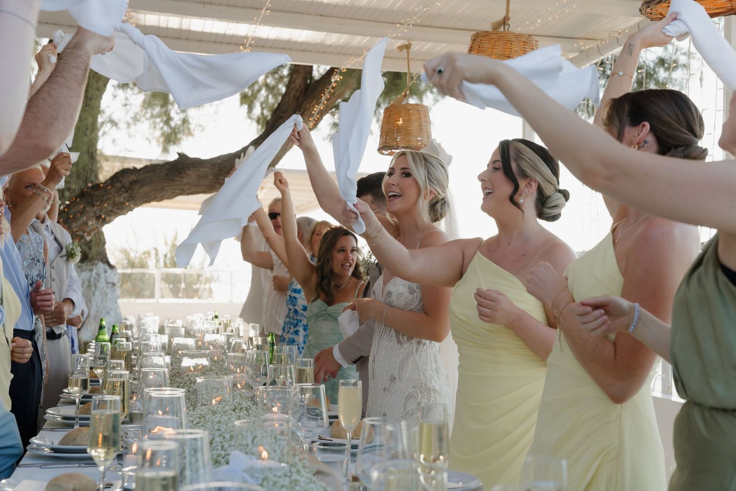 Wedding reception celebration with guests raising glasses in a toast under outdoor canopy.
