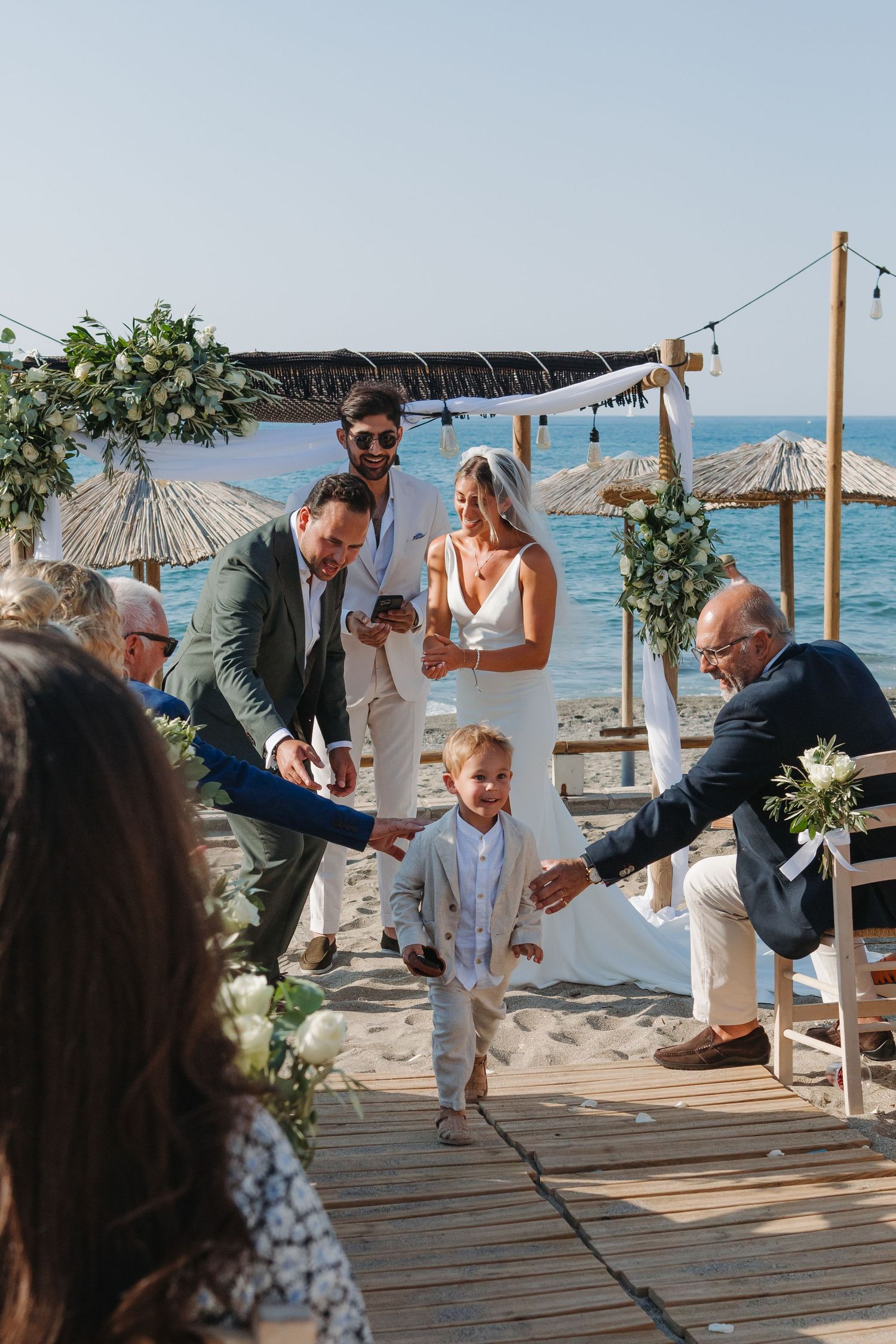 A joyful beach wedding ceremony moment with guests celebrating on a wooden deck by the ocean.