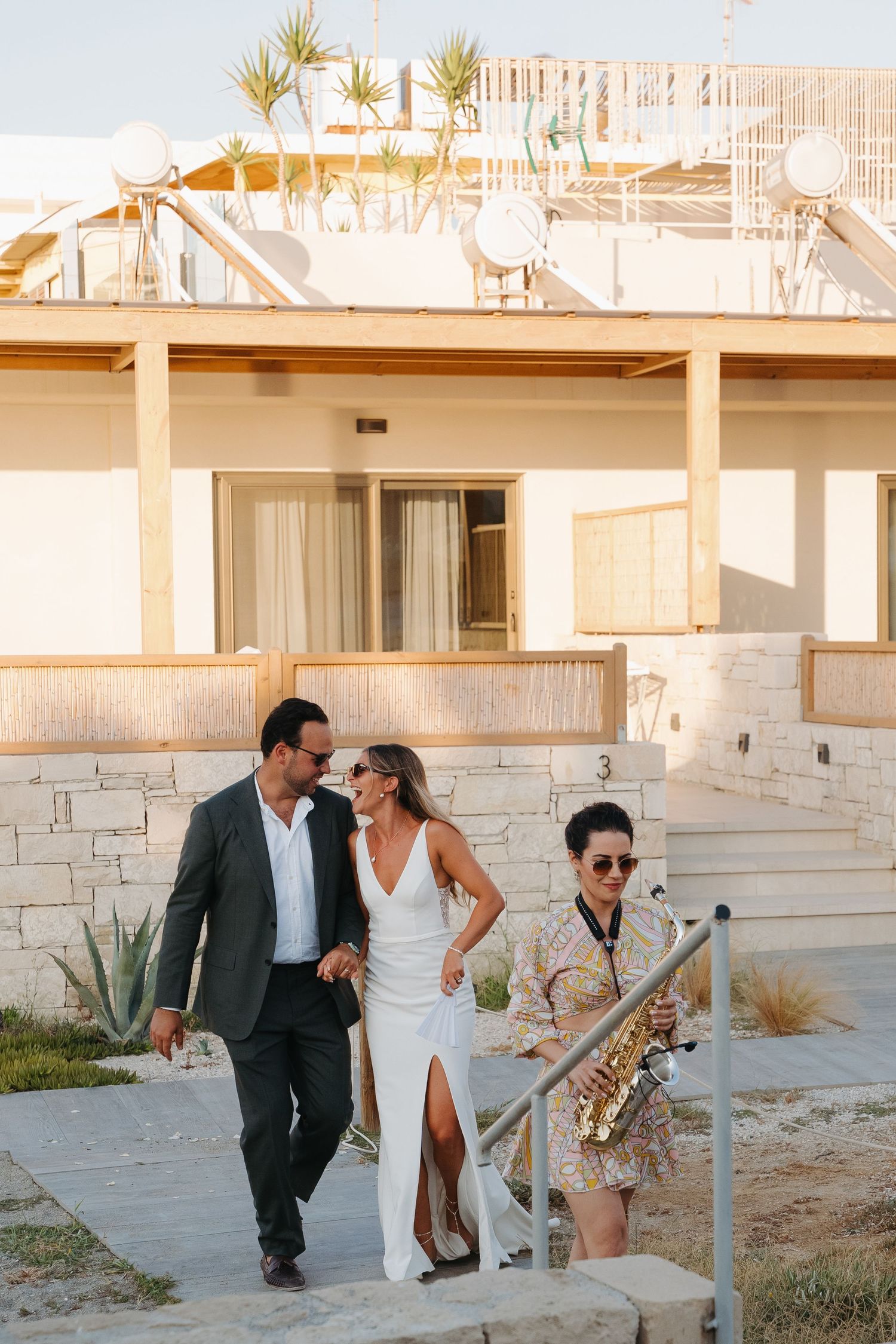 Wedding party walking and laughing together outside a modern stone building.