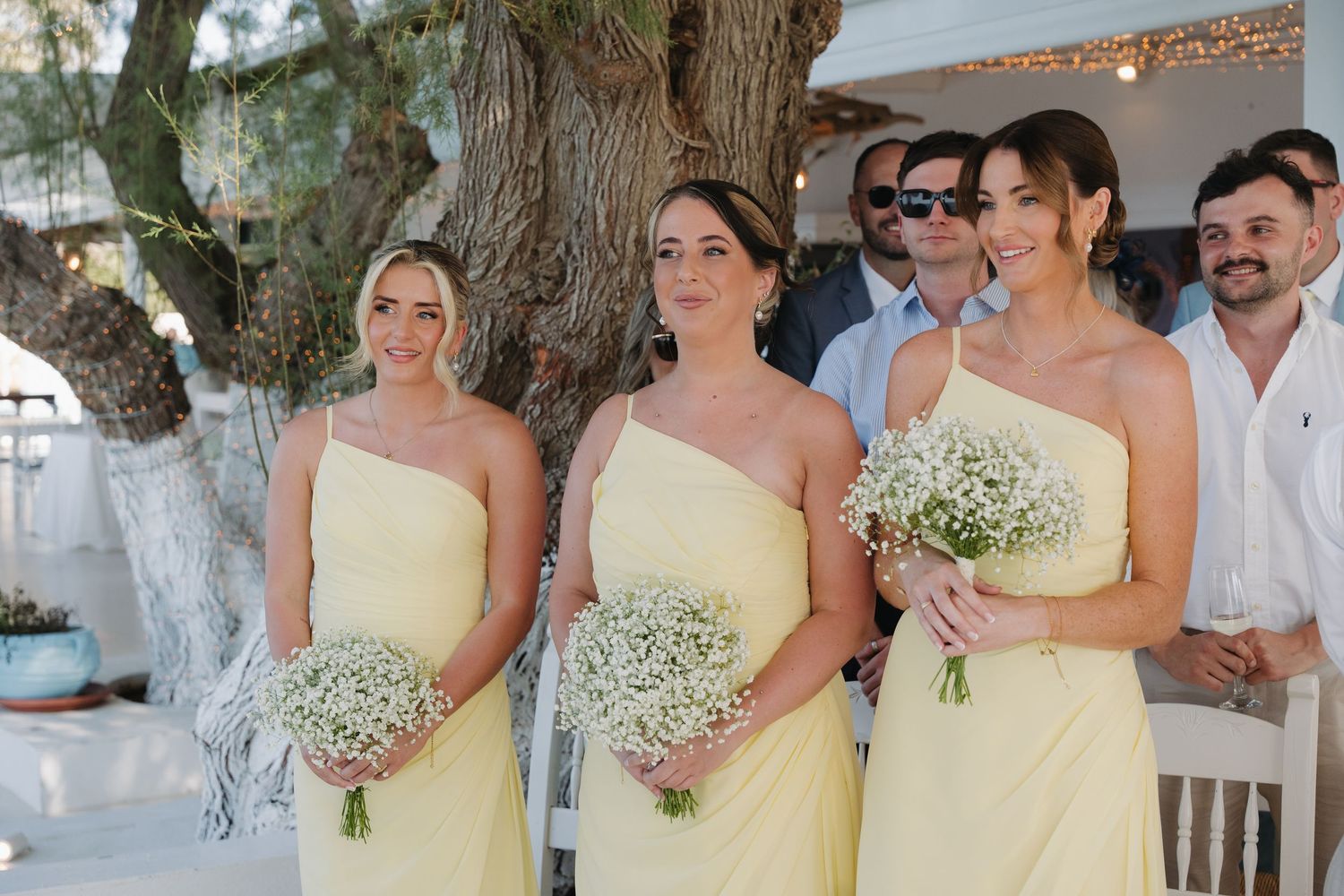 Wedding party in coordinated pale yellow dresses holding baby's breath bouquets.