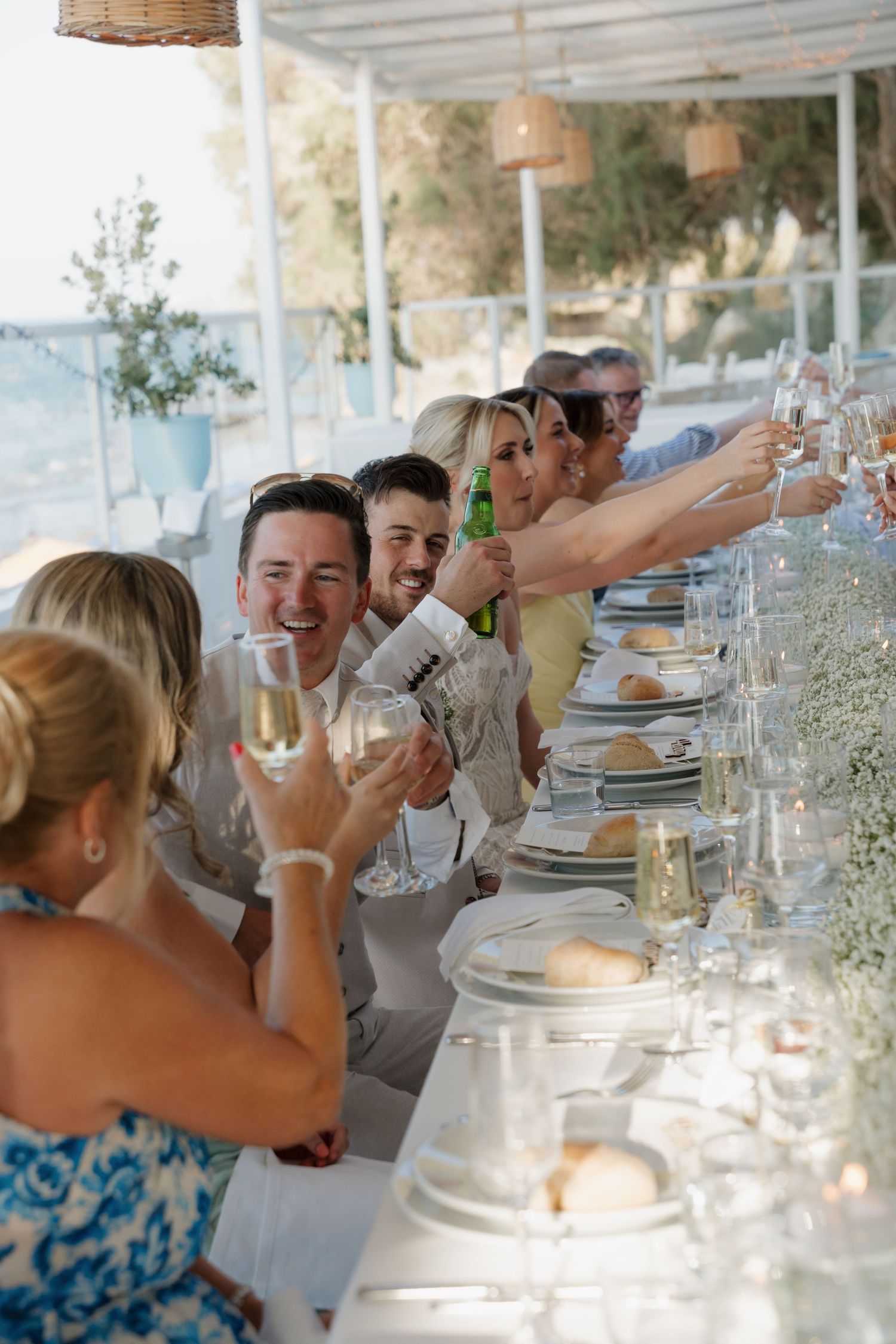 Wedding reception table setup with glassware and guests celebrating at a seaside venue.