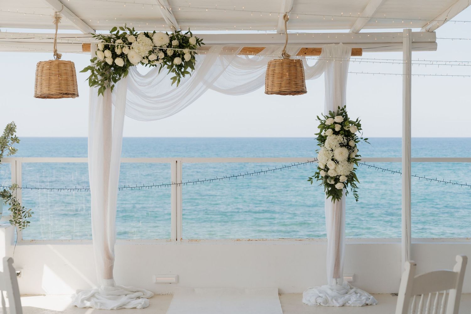 Romantic beach wedding ceremony setup with white draping and floral arrangements.