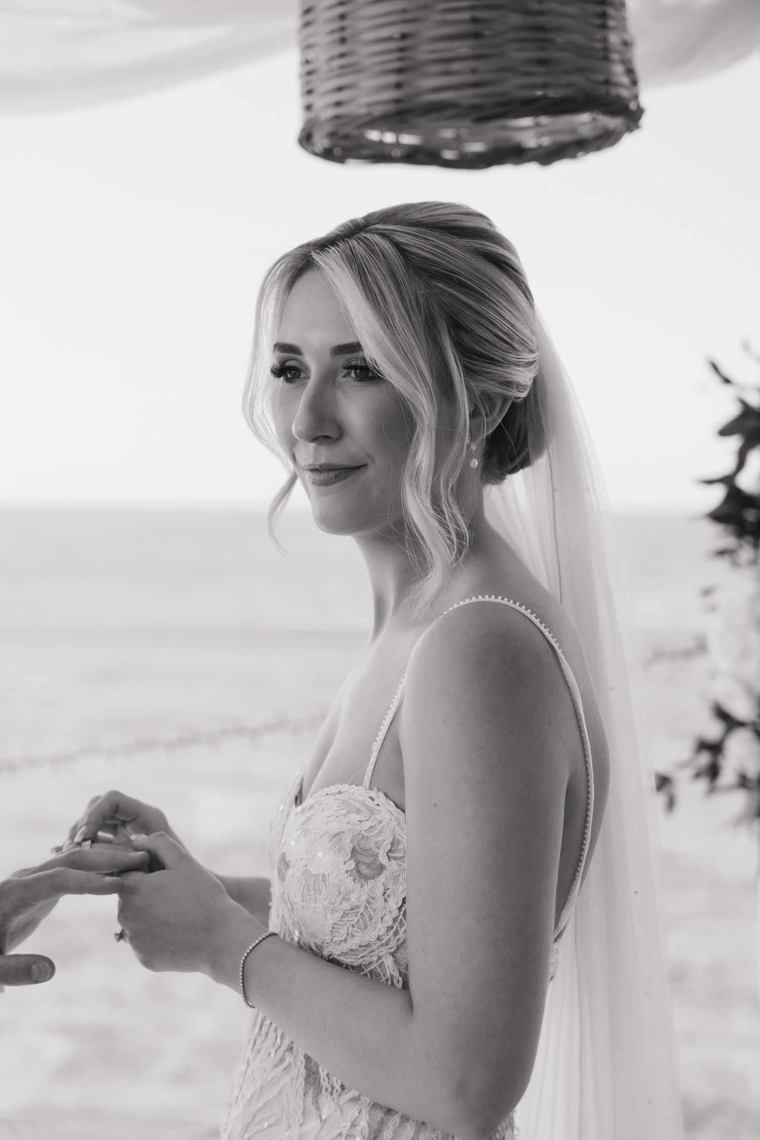 A bride in a lace wedding dress smiles during a seaside ceremony with white draping in the background.