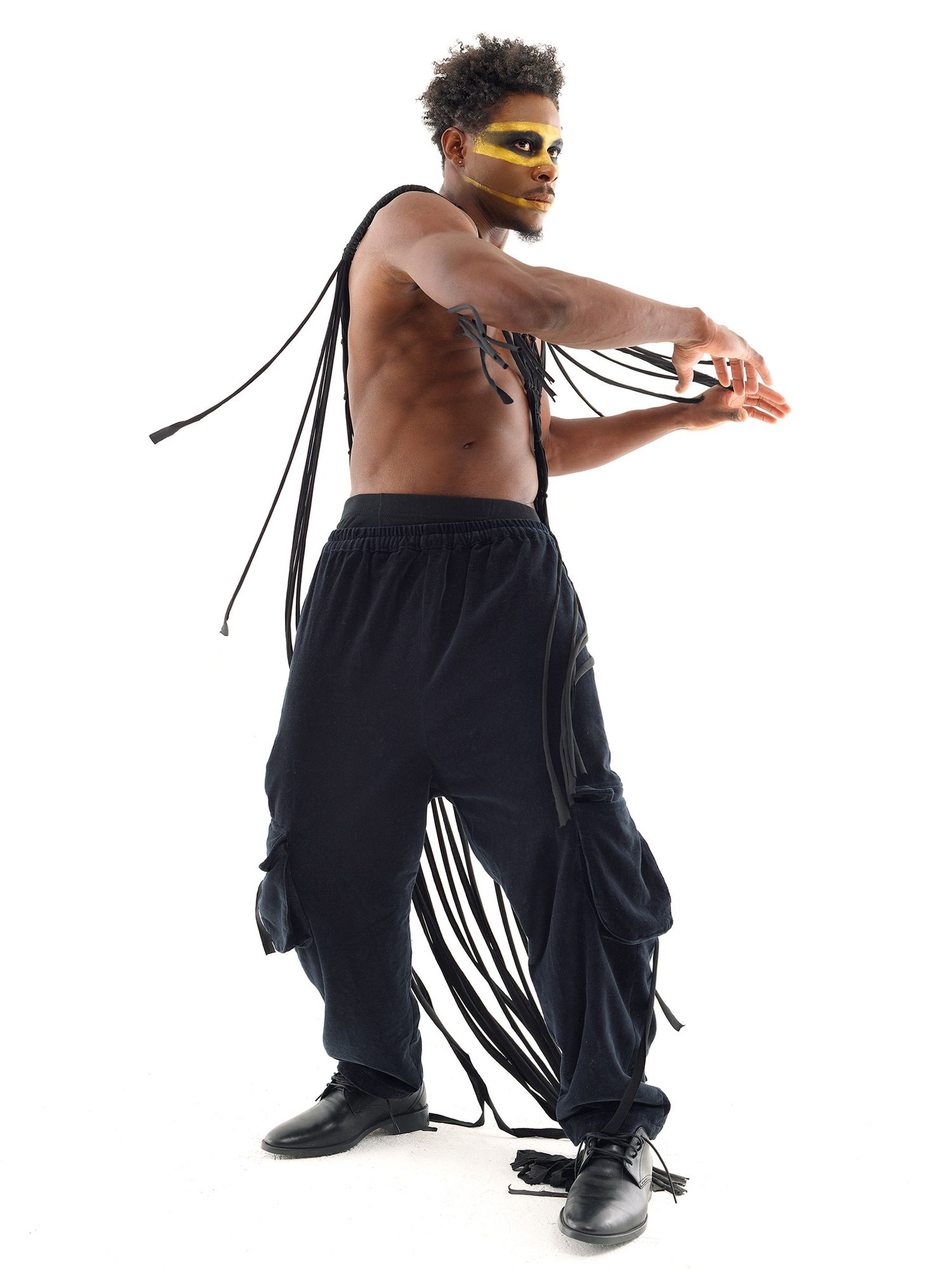Performer in black cargo pants and yellow sunglasses strikes a dance pose against white background with flowing ribbons.
