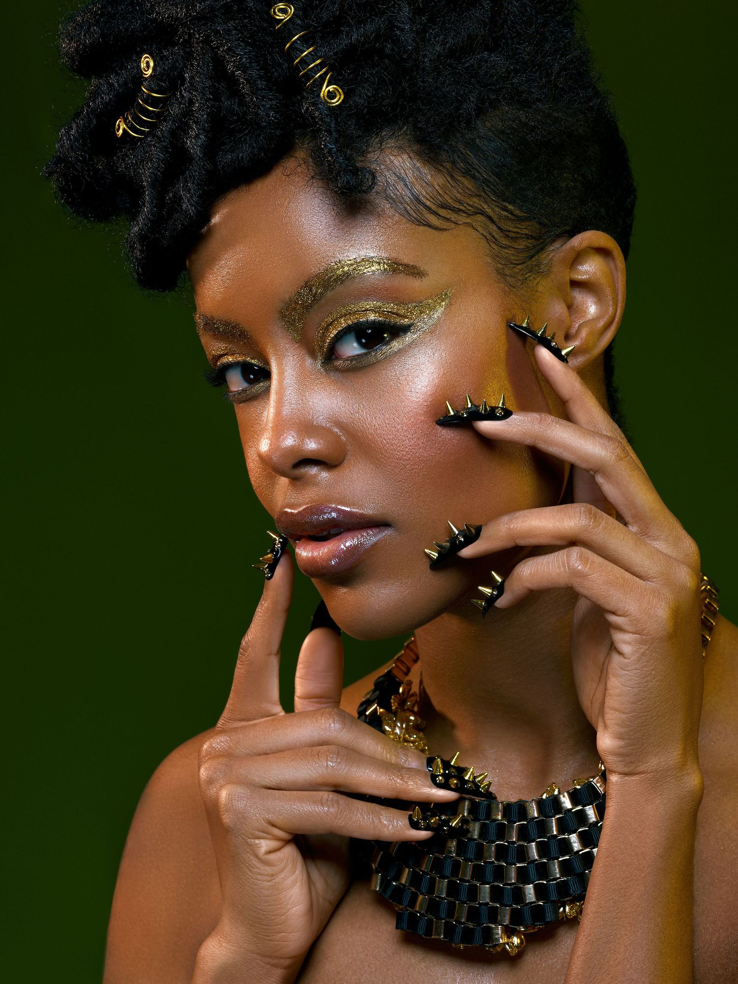 Beauty portrait with gold glitter eye makeup and statement black necklace against dark green background.