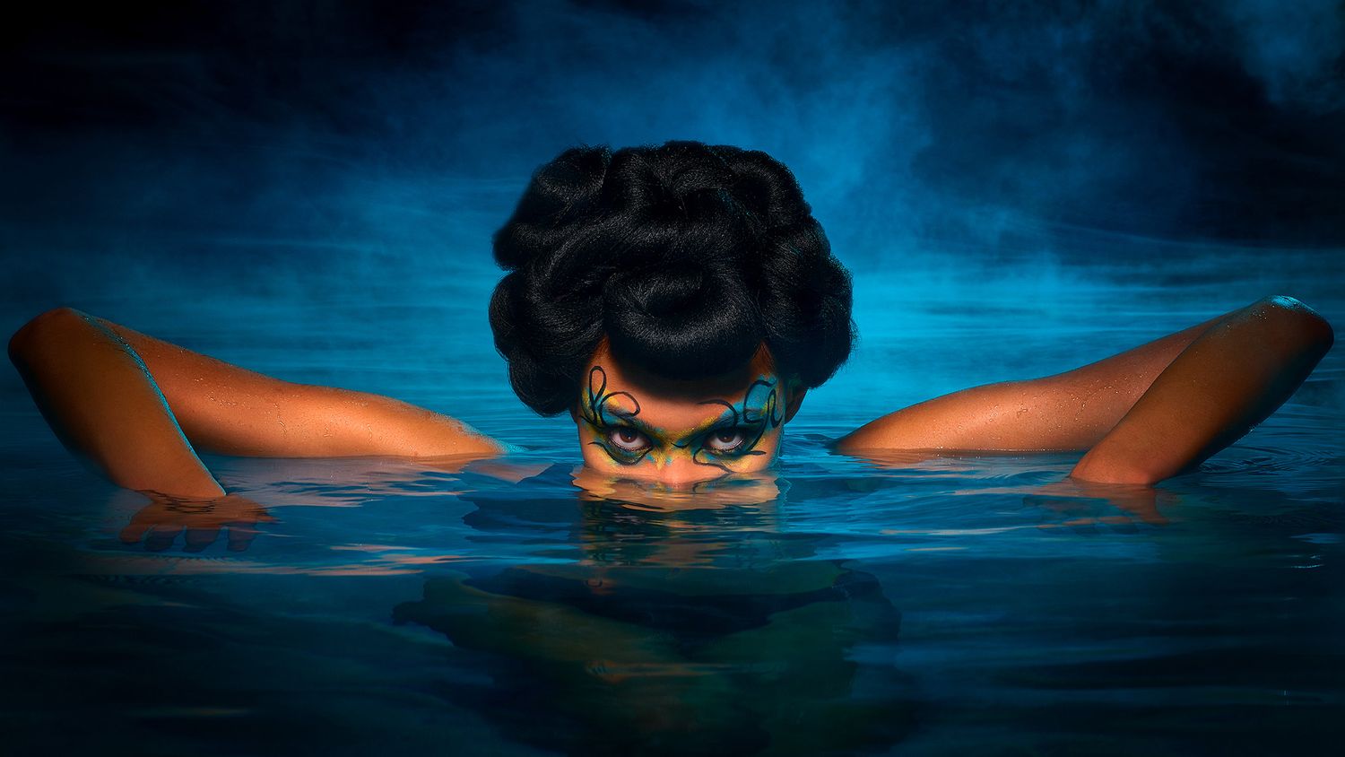 Person swimming underwater in dark blue pool with eyes visible above water creating dramatic reflection.