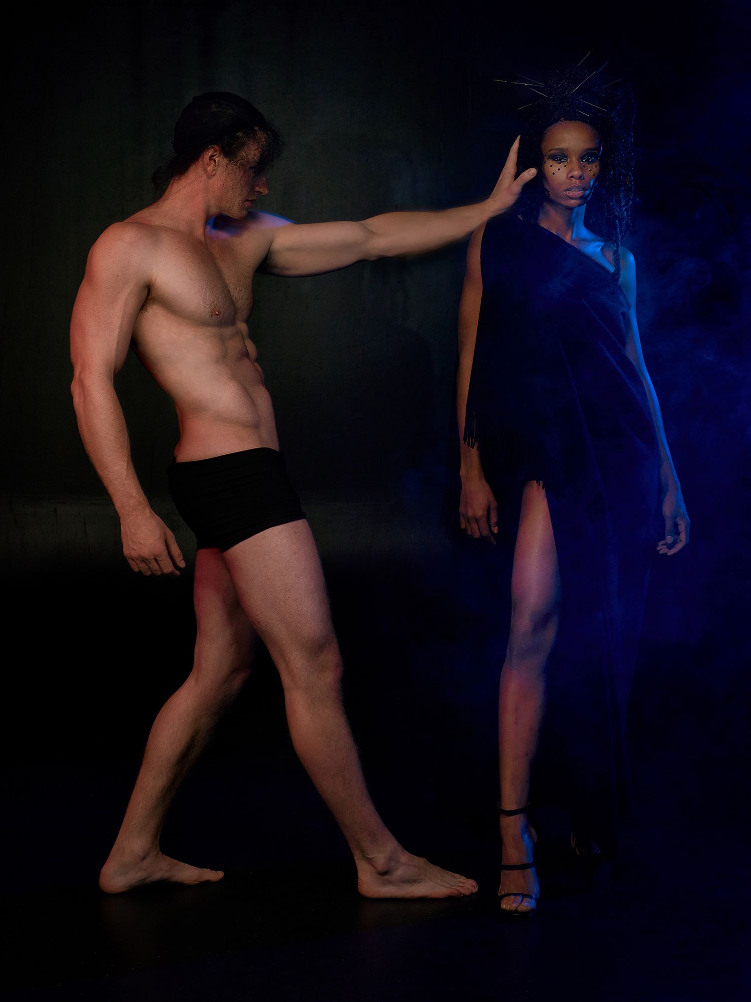 Dramatic fashion photo with contrasting lighting showing two models in minimal dark attire.