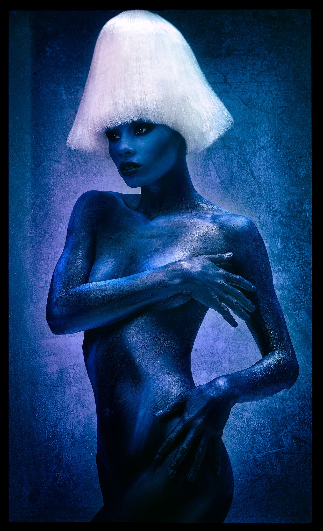 Artistic portrait with blue body paint and white geometric bob haircut against dark background in surreal style.