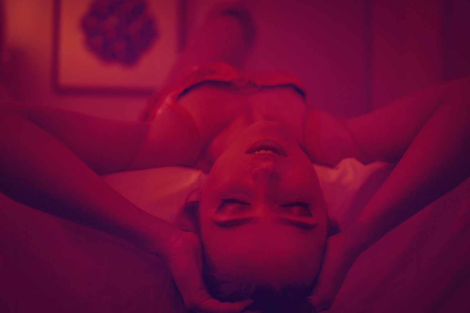 Person lying down in a room bathed in dramatic red lighting viewed from above perspective.