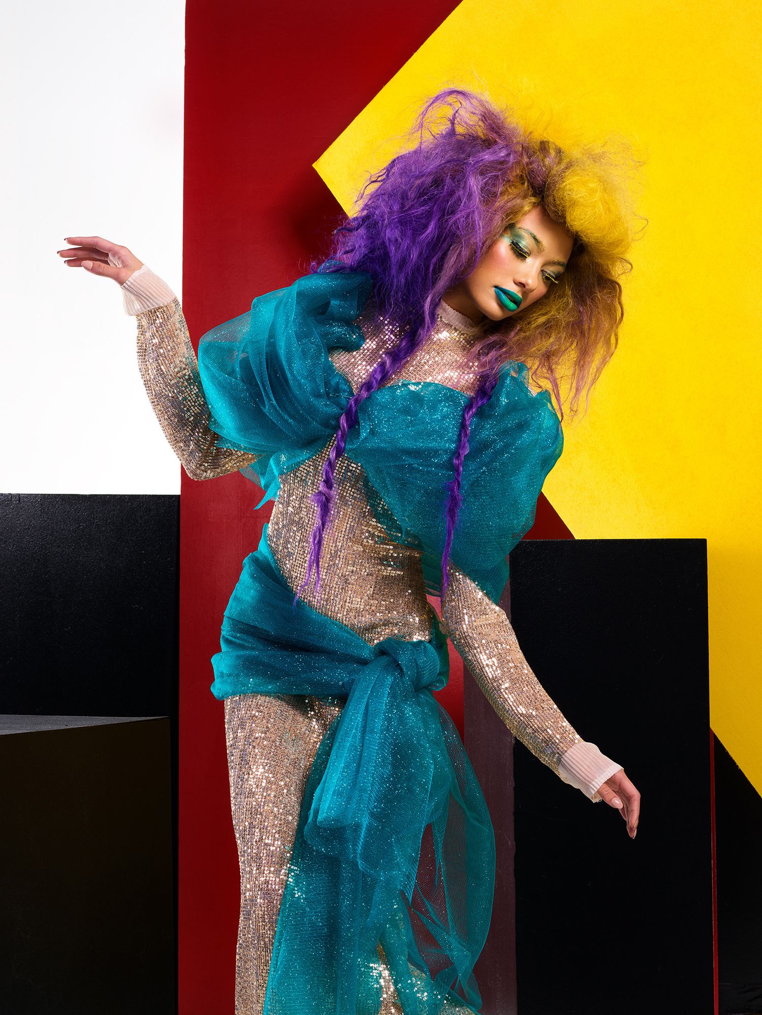 Artistic fashion shot with model in turquoise and sparkly outfit against colorful geometric backdrop.