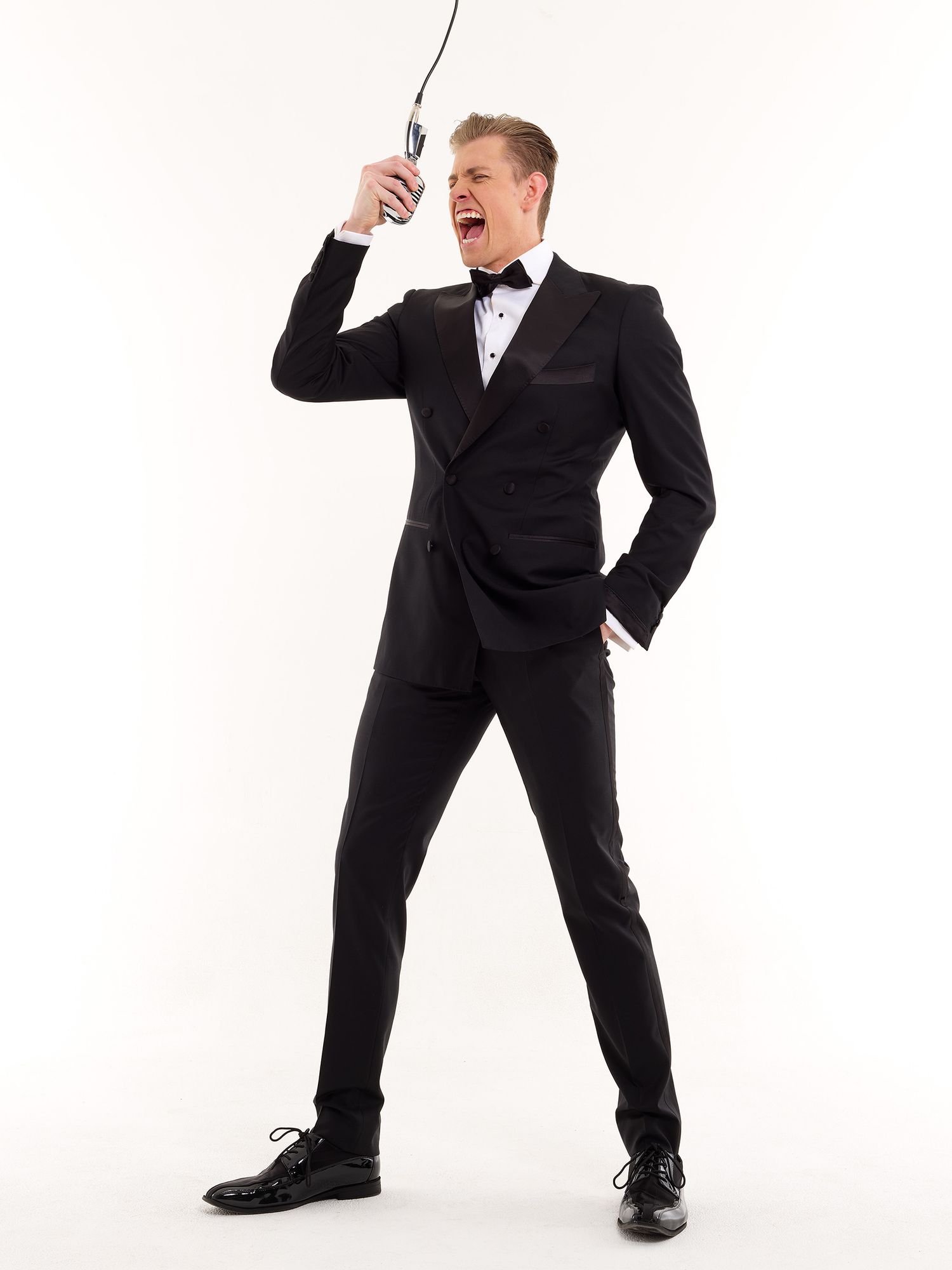 Professional wearing black tuxedo strikes an energetic pose against white background.
