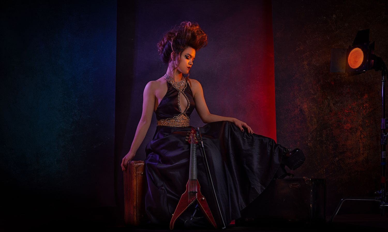 A woman in a flowing dark gown poses against dramatic blue and red lighting on stage.