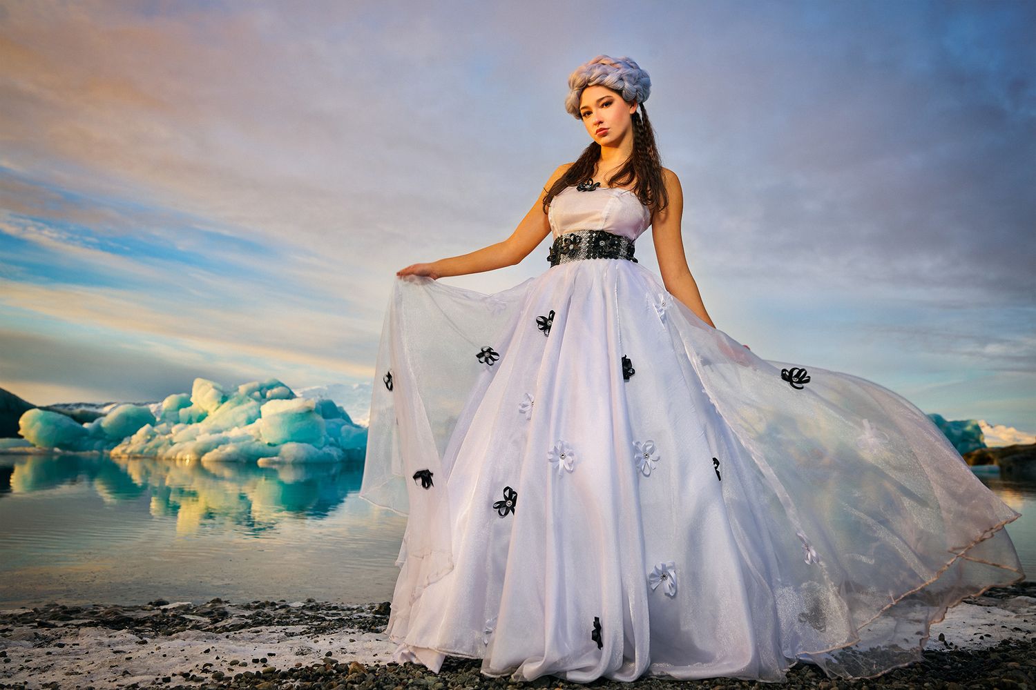 A flowing white wedding dress photographed against a dramatic backdrop of glaciers and mountains in a remote landscape.