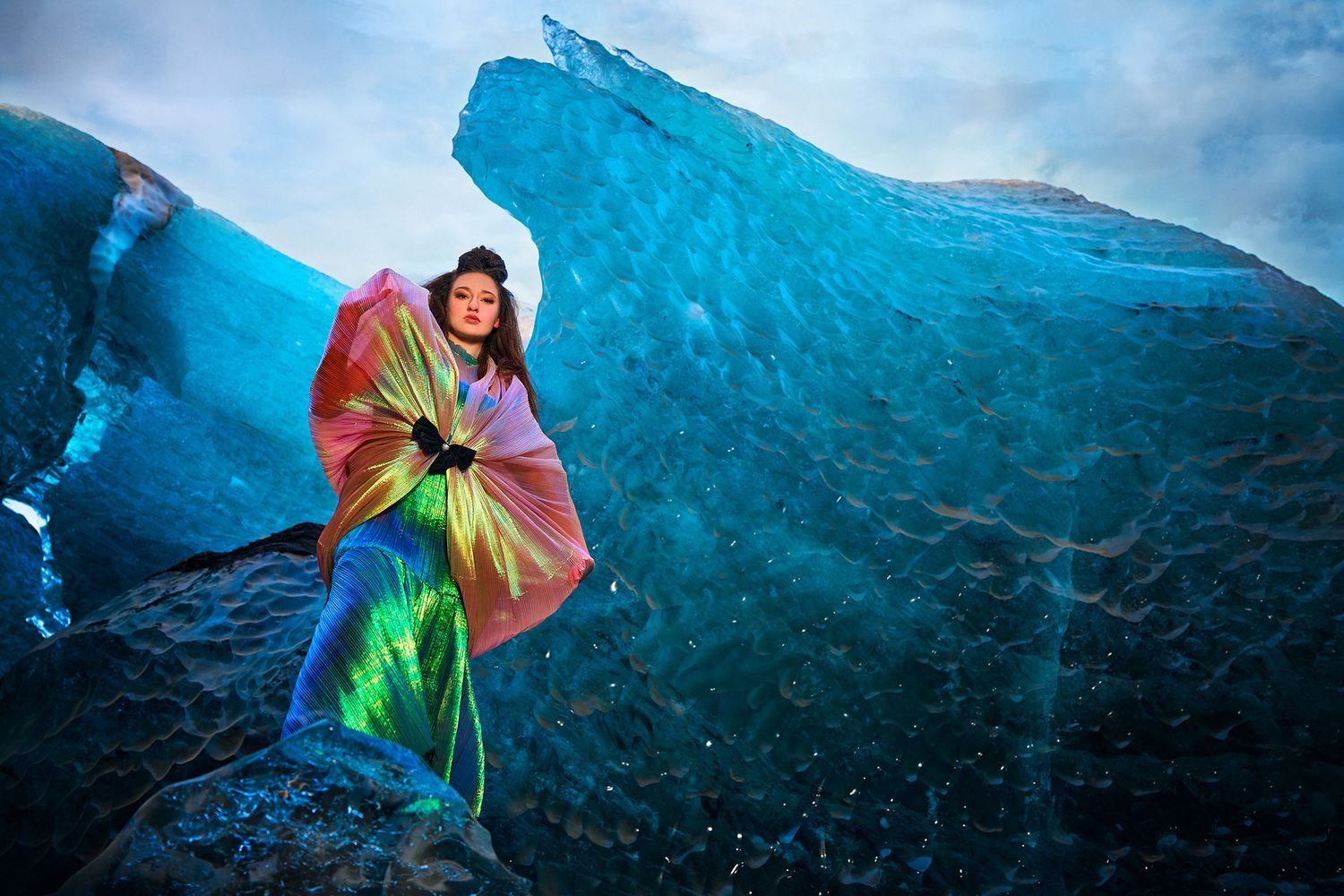 A colorful rainbow umbrella contrasts against the blue ice formations of a glacier landscape.