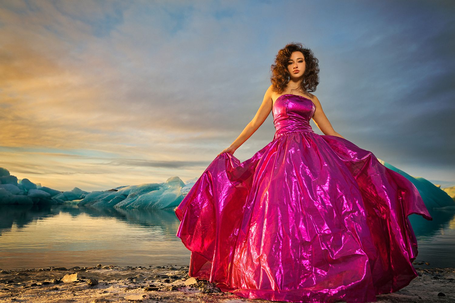 A flowing magenta gown billows dramatically against a sunset mountain landscape with dramatic clouds and reflective water.